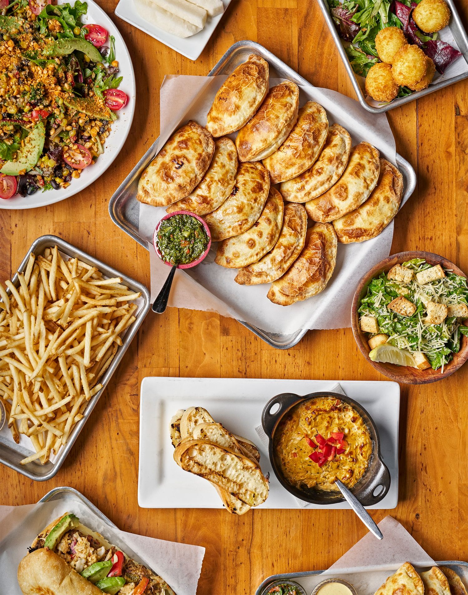 Overhead view of restaurant table with pot stickers, french fries, salads and various dishes on wooden surface.