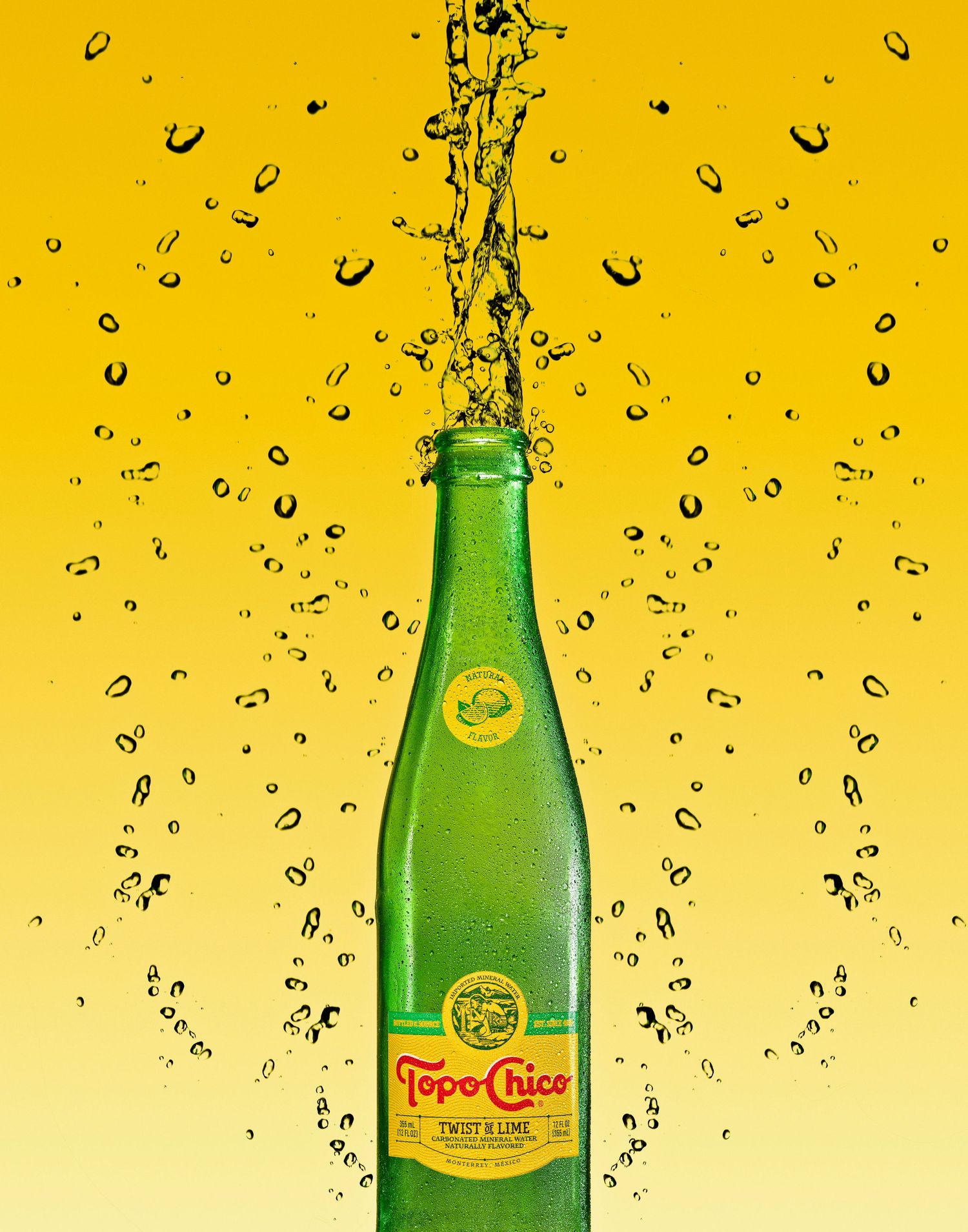 Topo Chico glass bottle with water droplets splashing against yellow background.