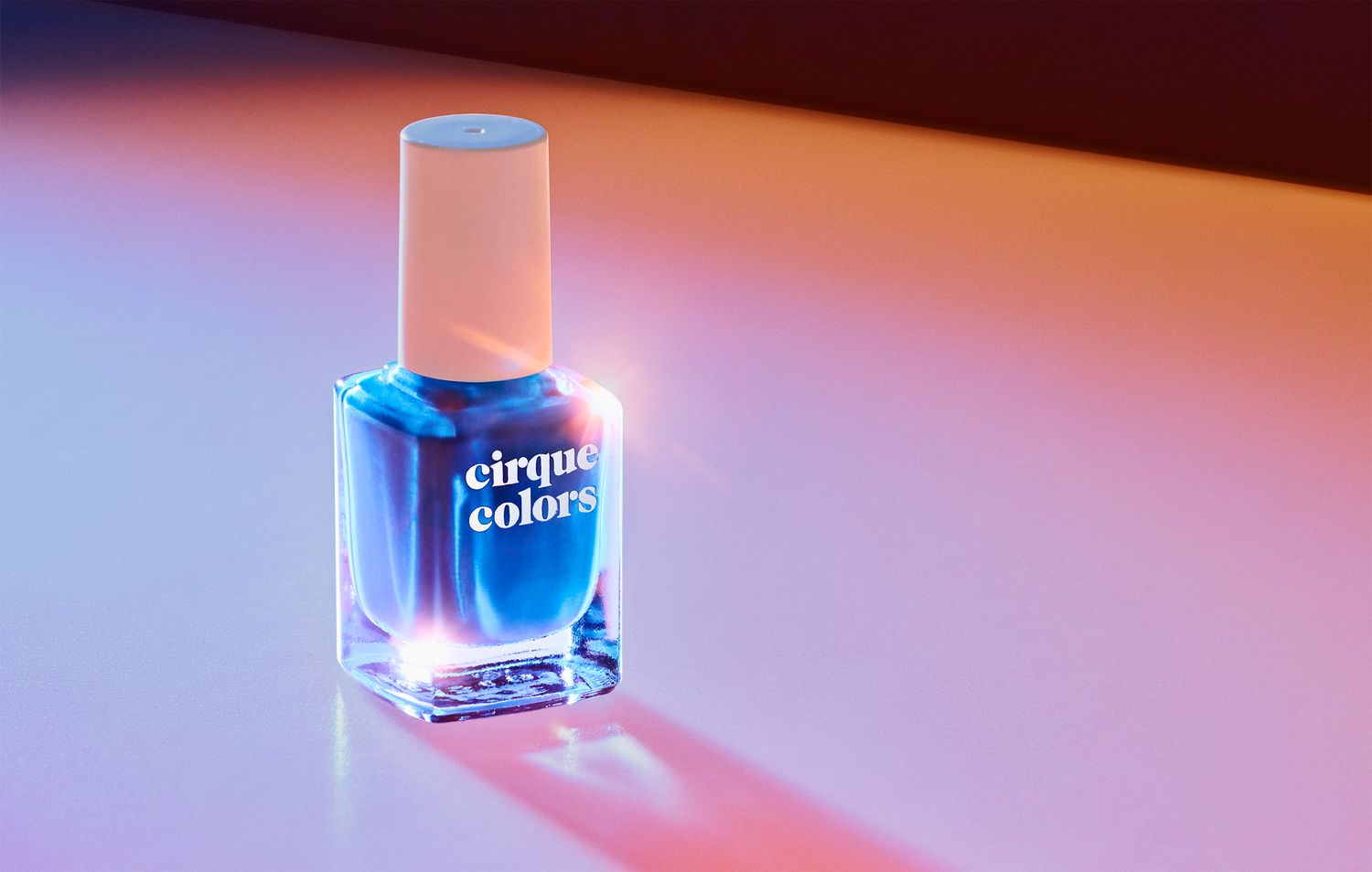 Glass nail polish bottles casting colorful shadows in a gradient sequence from pink to blue lighting.