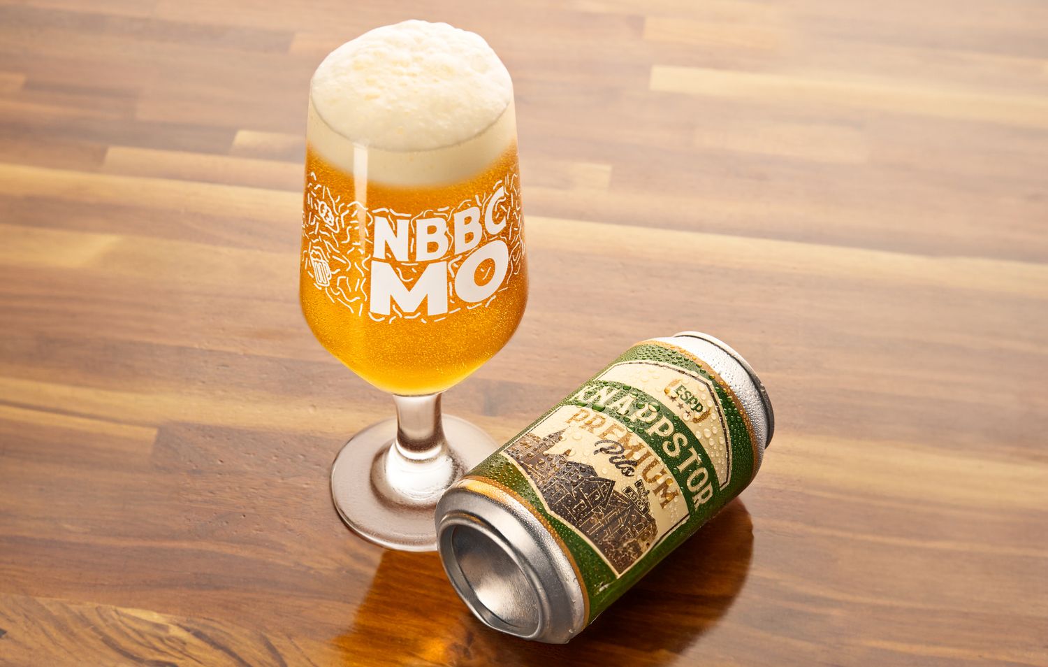 Glass of craft beer next to aluminum can on wooden table surface.