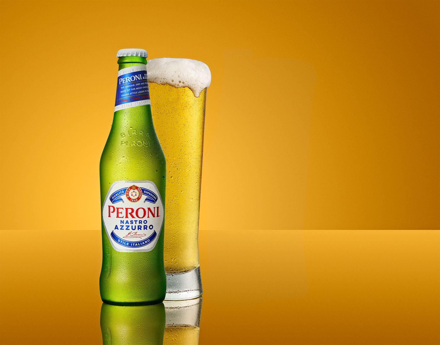Peroni Nastro Azzurro beer bottle beside a full glass of lager on a golden yellow background.