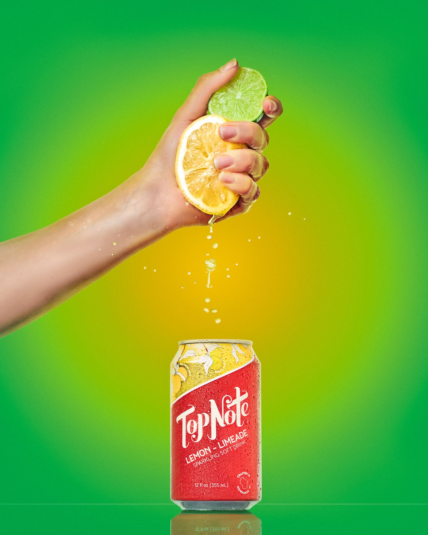 Hand squeezing lemon over a red Topo Chico can against green background.