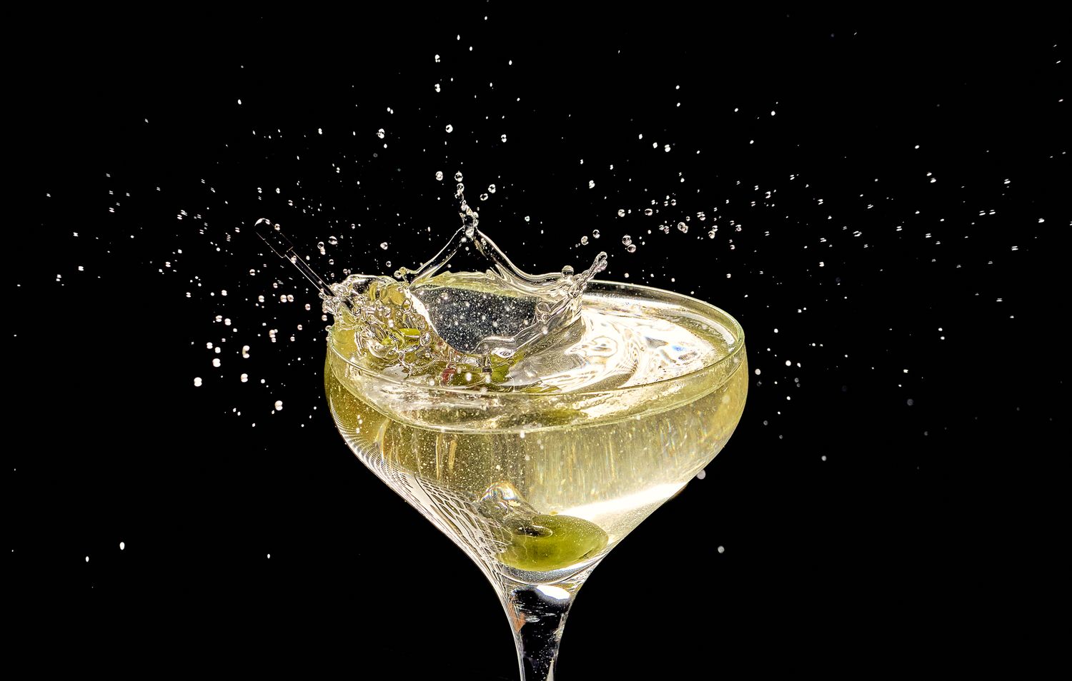 Splashing liquid in martini glass creating dynamic droplets against black background.