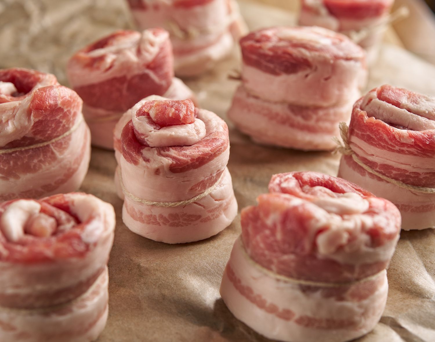 Raw beef pinwheels wrapped in bacon arranged on parchment paper.