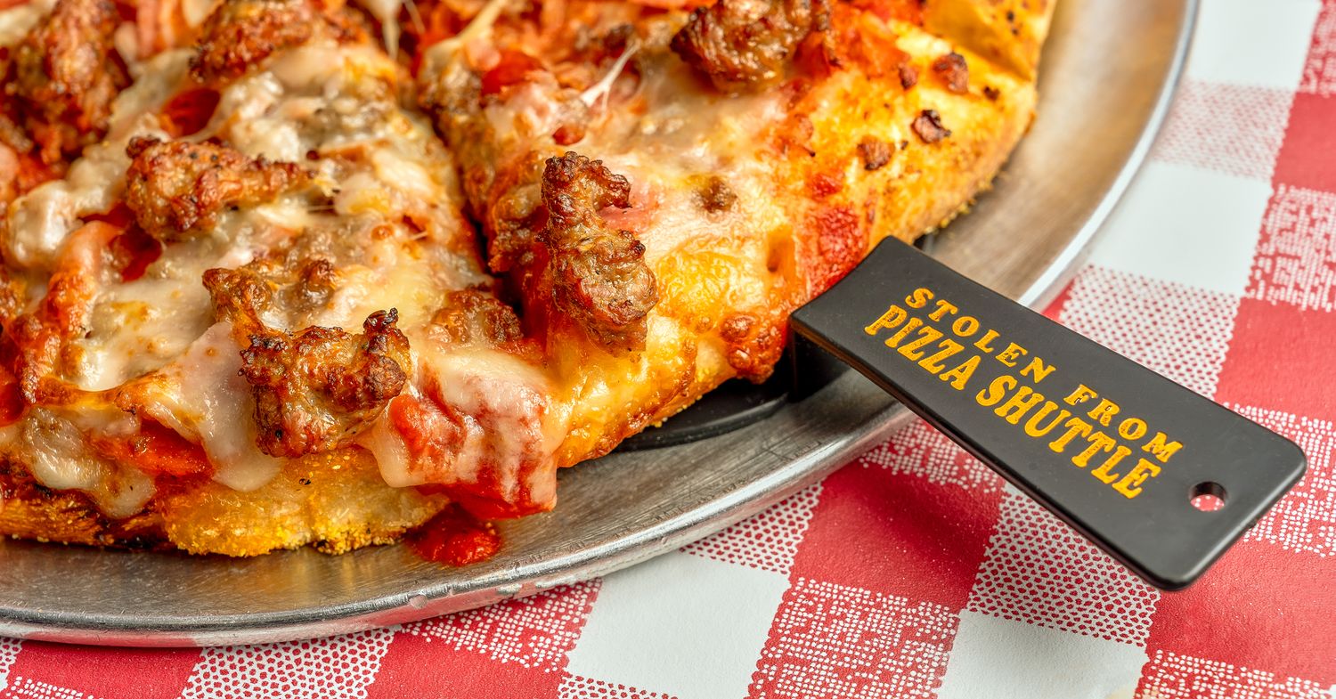 Hot sausage pizza on red checkered tablecloth with a pizza spatula reading, 