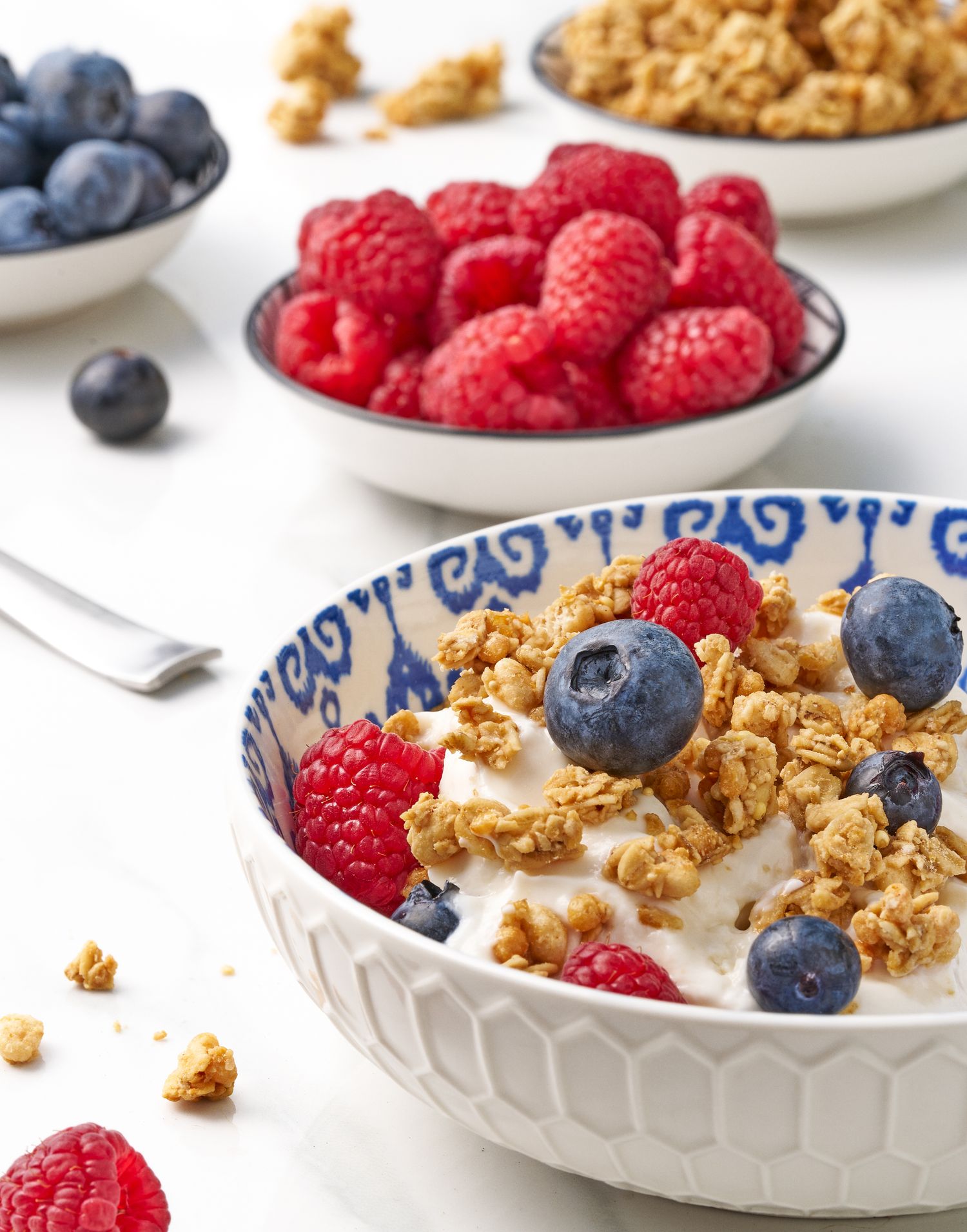 Bowl of yogurt topped with fresh raspberries, blueberries and crunchy granola on white background.