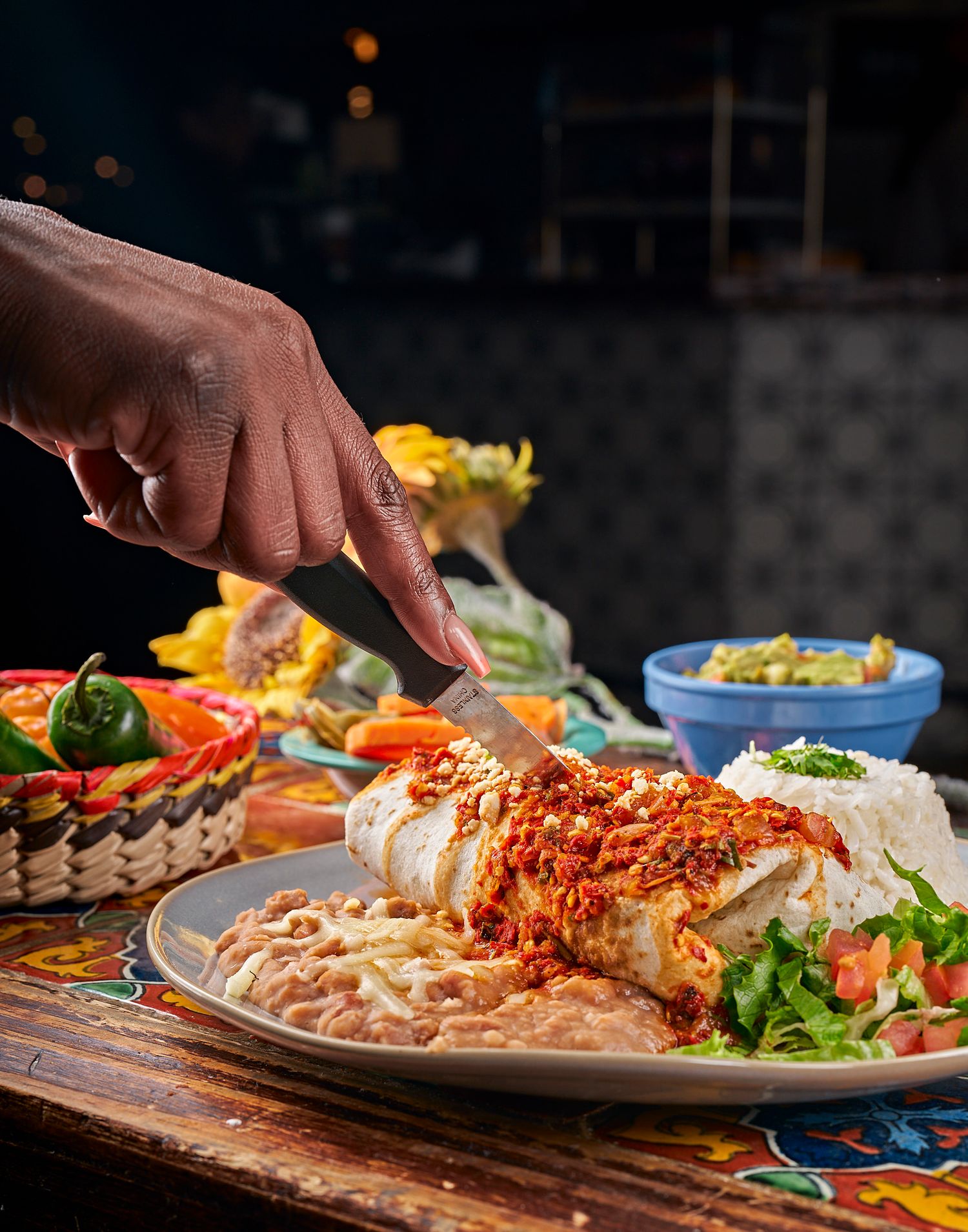 Hands garnishing colorful pasta dishes with red sauce and fresh herbs on dark plates.