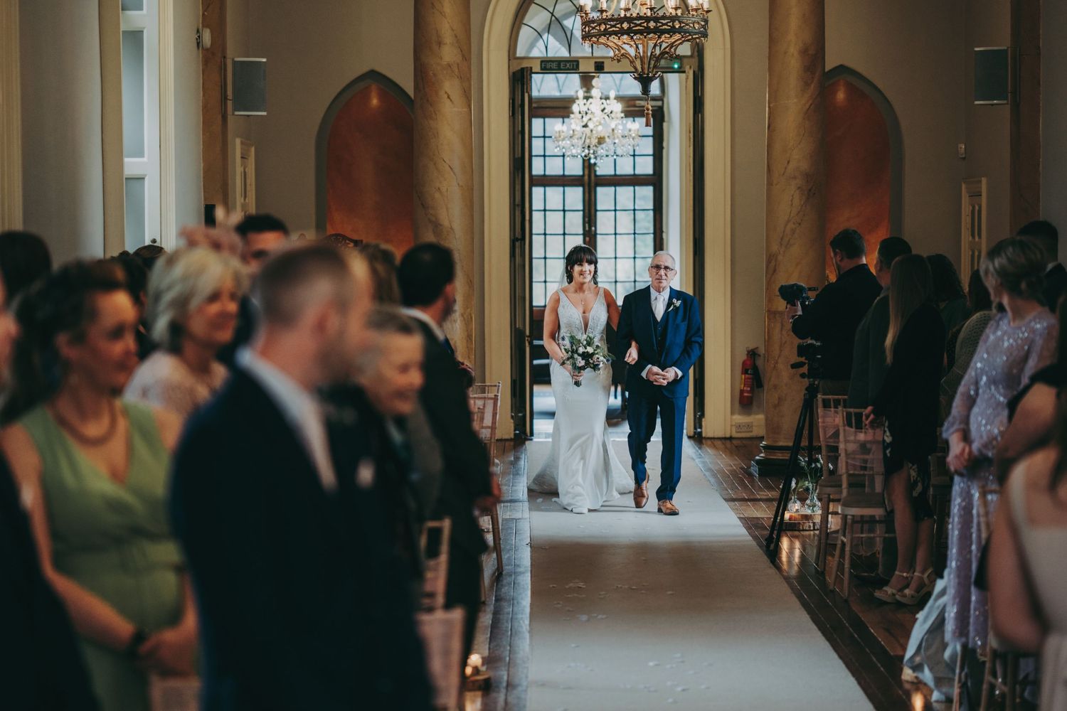 A wedding ceremony in an elegant hallway with guests lining both sides.