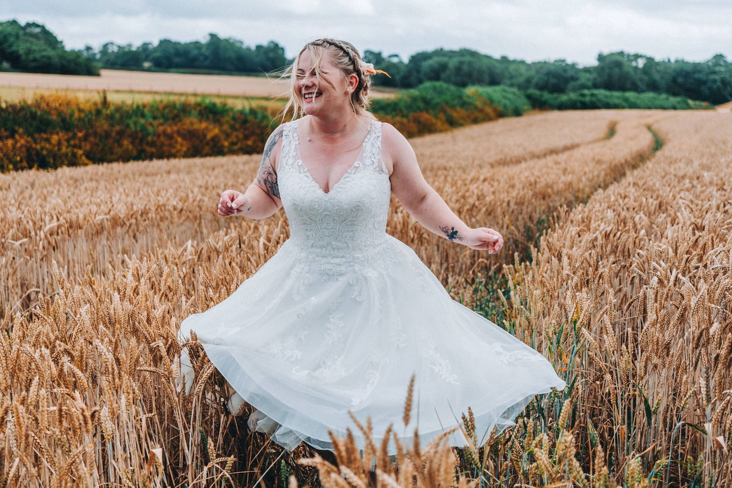 A joyful bride in a white lace dress twirls in a golden wheat field in Devon.