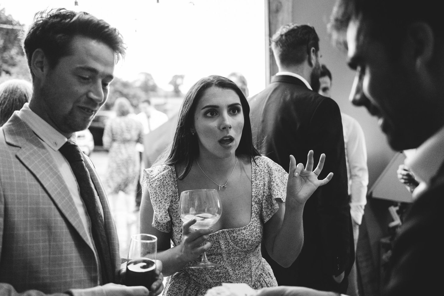 A woman in a sparkling dress animatedly chats with guests at an elegant black and white cocktail reception.
