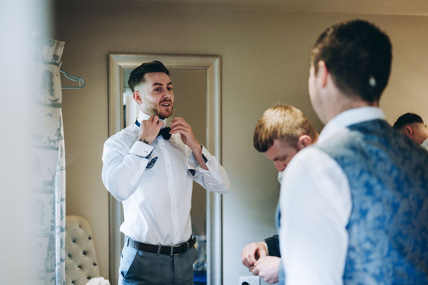 Several people in formalwear getting ready in a room with light walls and decorative elements.