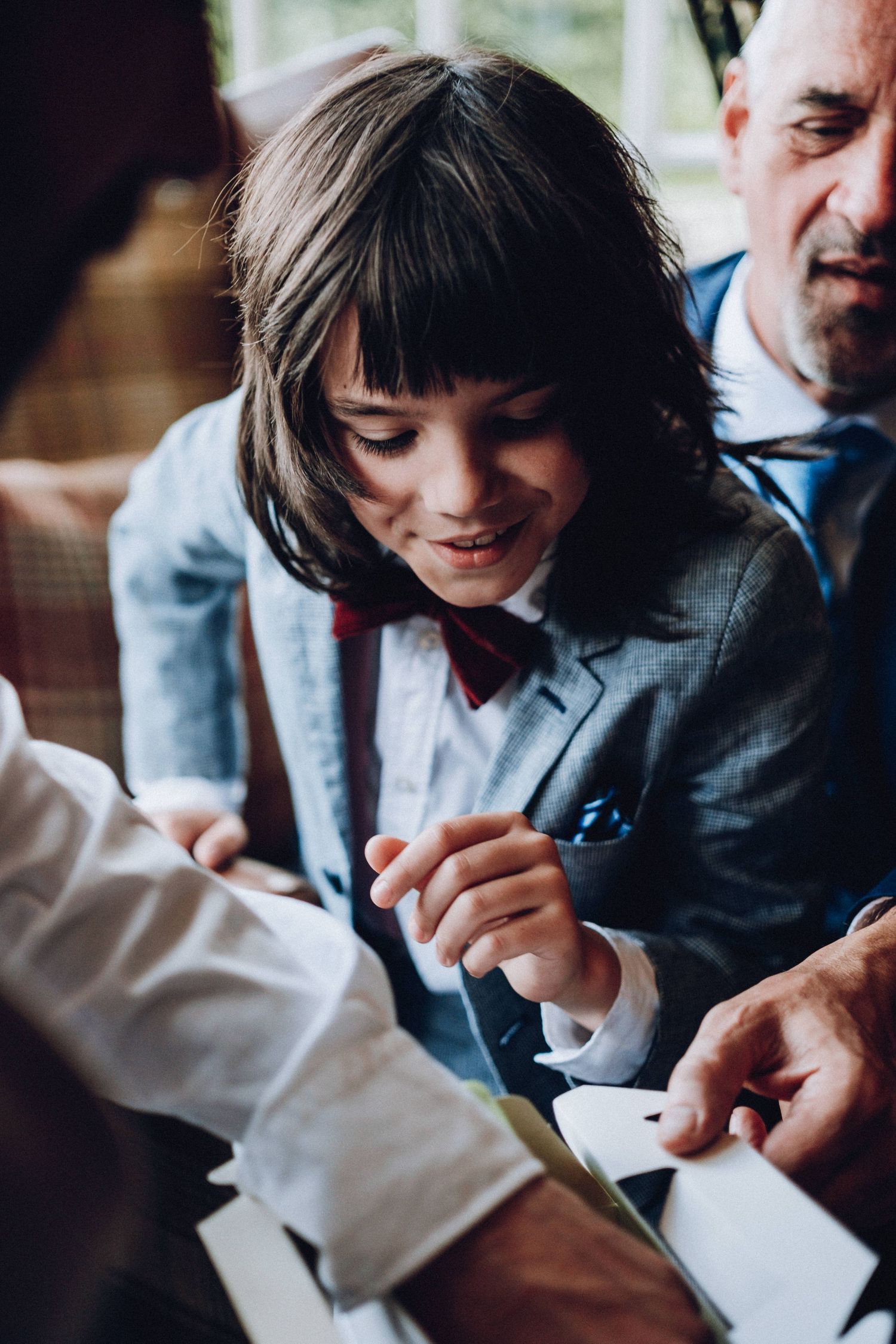 Child in a blue suit jacket looking down while playing with something in their hands.