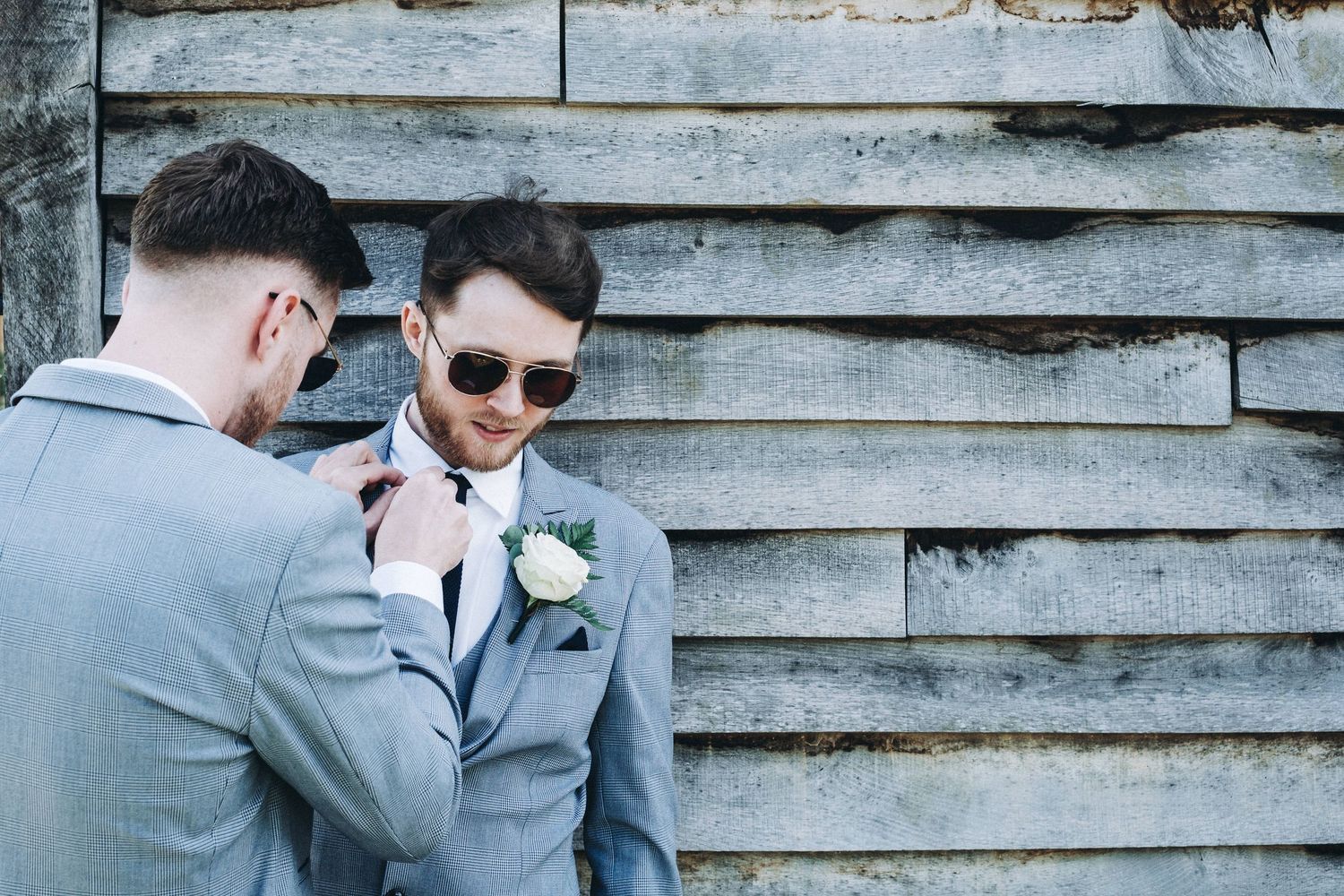 Wedding party in light blue suits gathered outside a rustic wooden building.