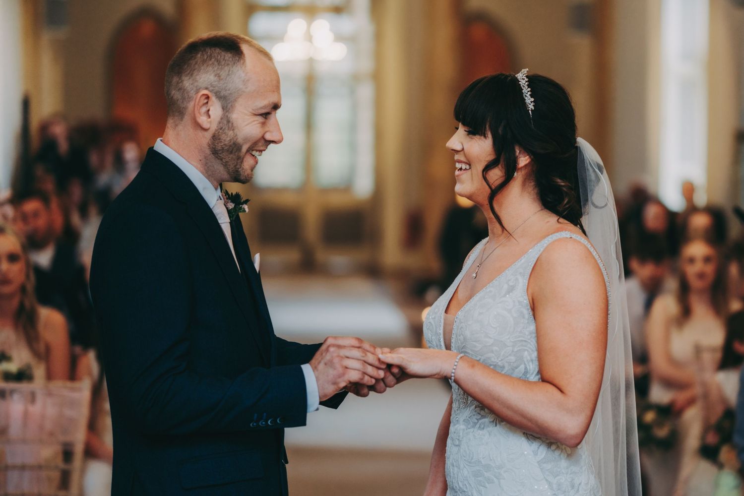 A joyful wedding ceremony moment as a couple exchanges rings in an elegant indoor venue.