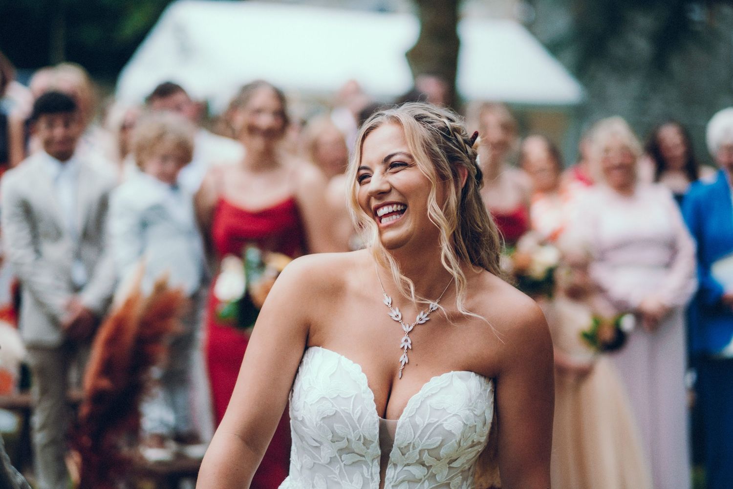 Bride in strapless white wedding dress laughing joyfully during outdoor celebration.