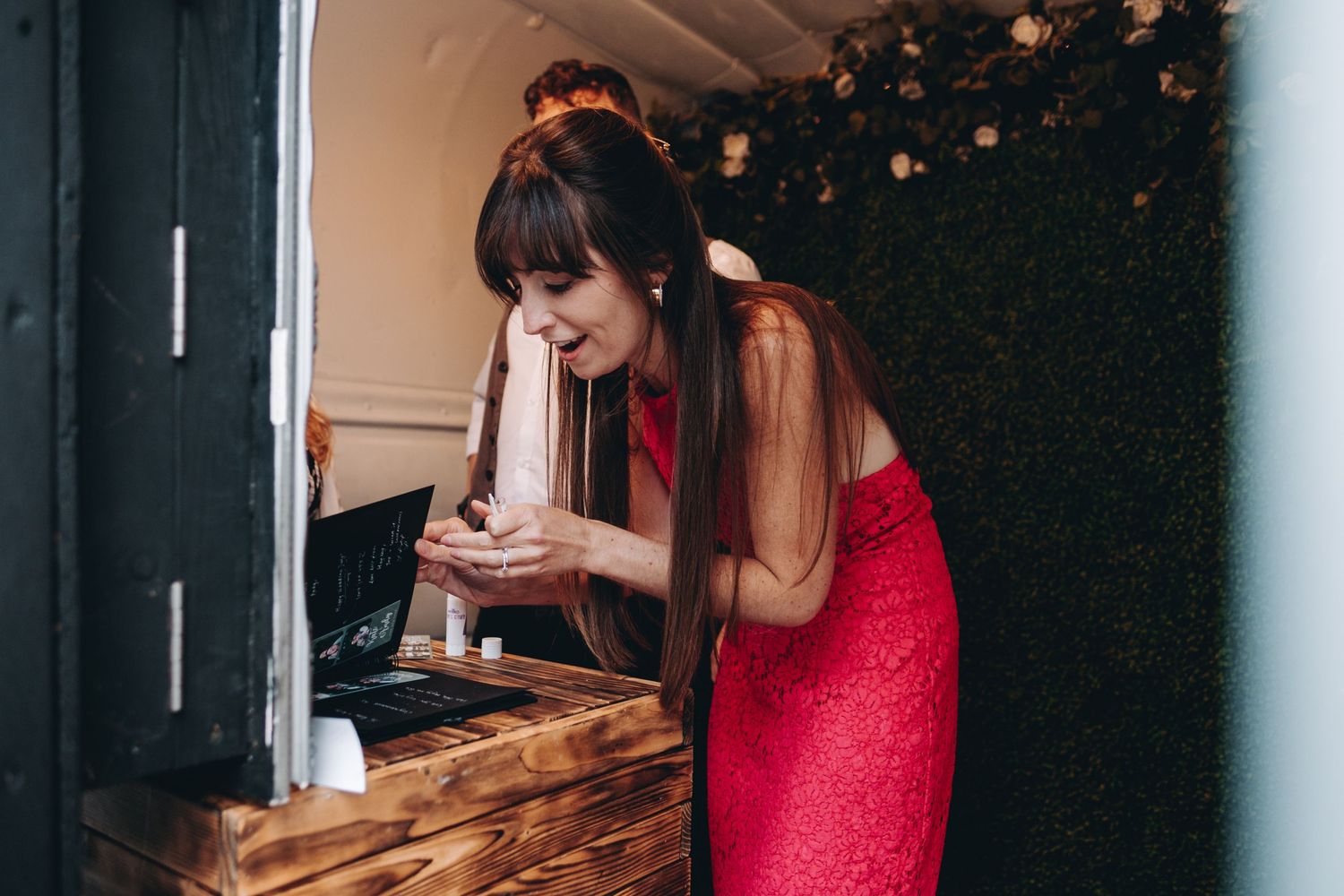 Someone in a sparkly red dress leans over a wooden surface while reading a phone in a dimly lit room.
