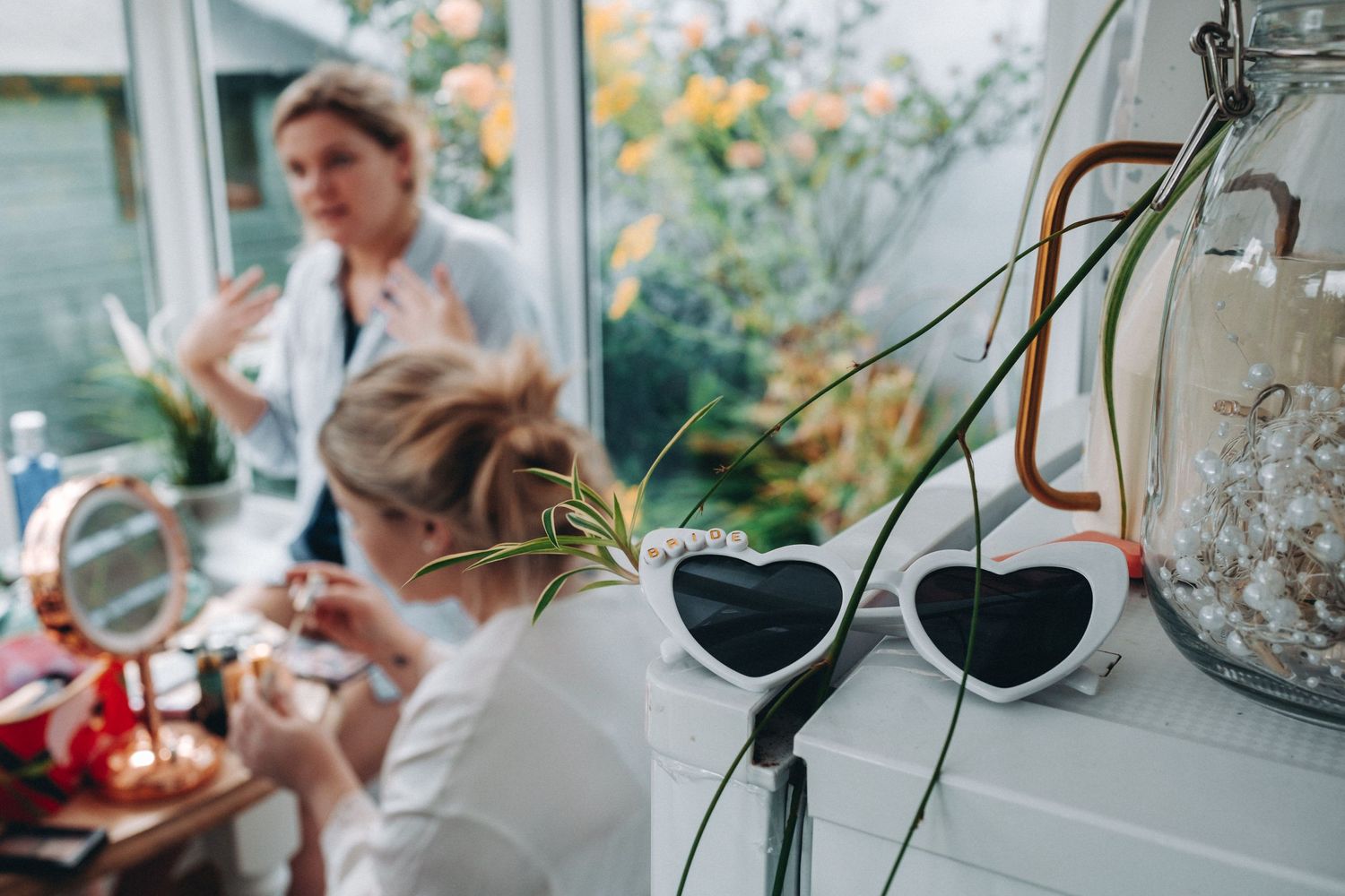 'Bride' glasses from Kates hen party in the foreground with kate and her bridesmaid applying makeup in the background.