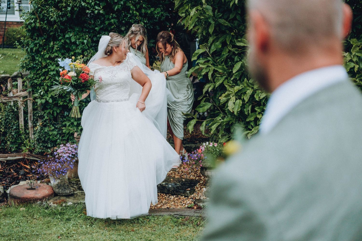 A bride in a white dress walks through a beautiful garden setting during a summer wedding.