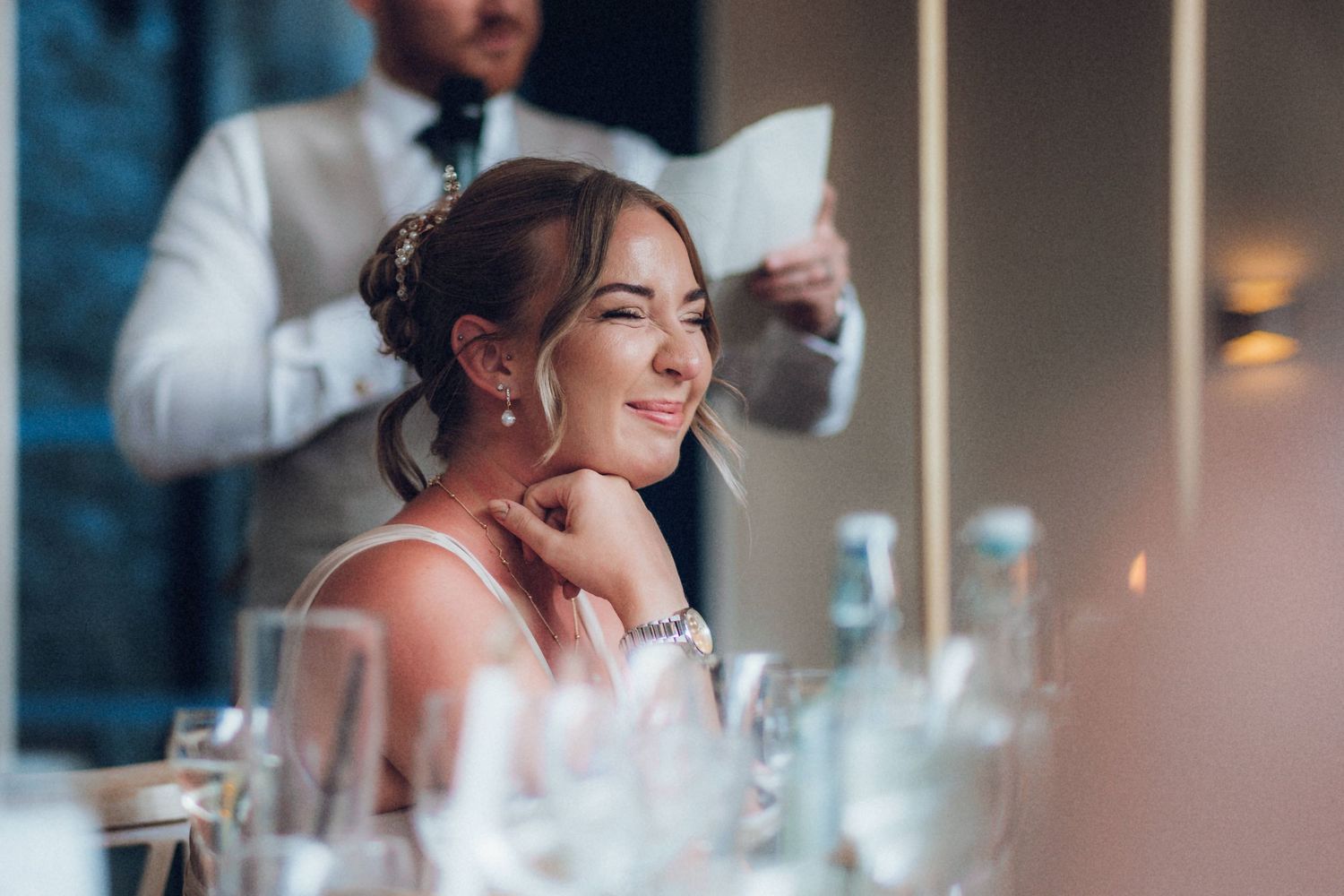 A guest smiling during wedding reception speeches while seated at decorated table.