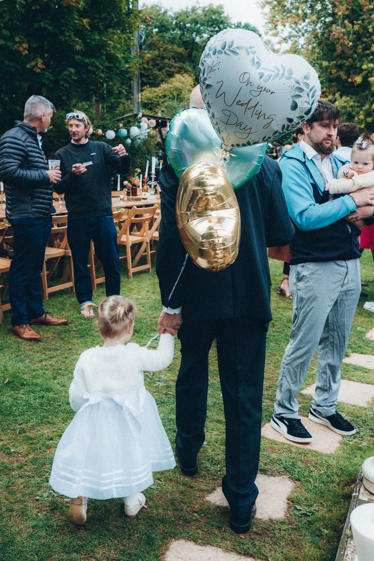 Wedding guests gather on grass with gold heart-shaped balloons during outdoor celebration.