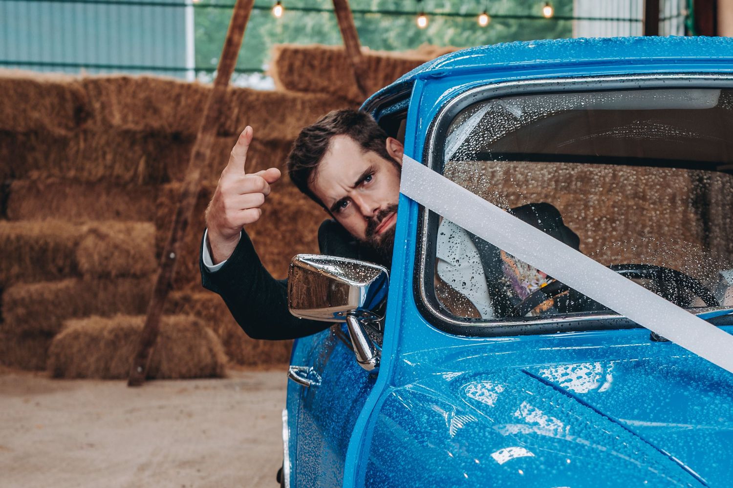 groom hangs out of a bright blue mini window with a thumbs up gesture against a brown wall.