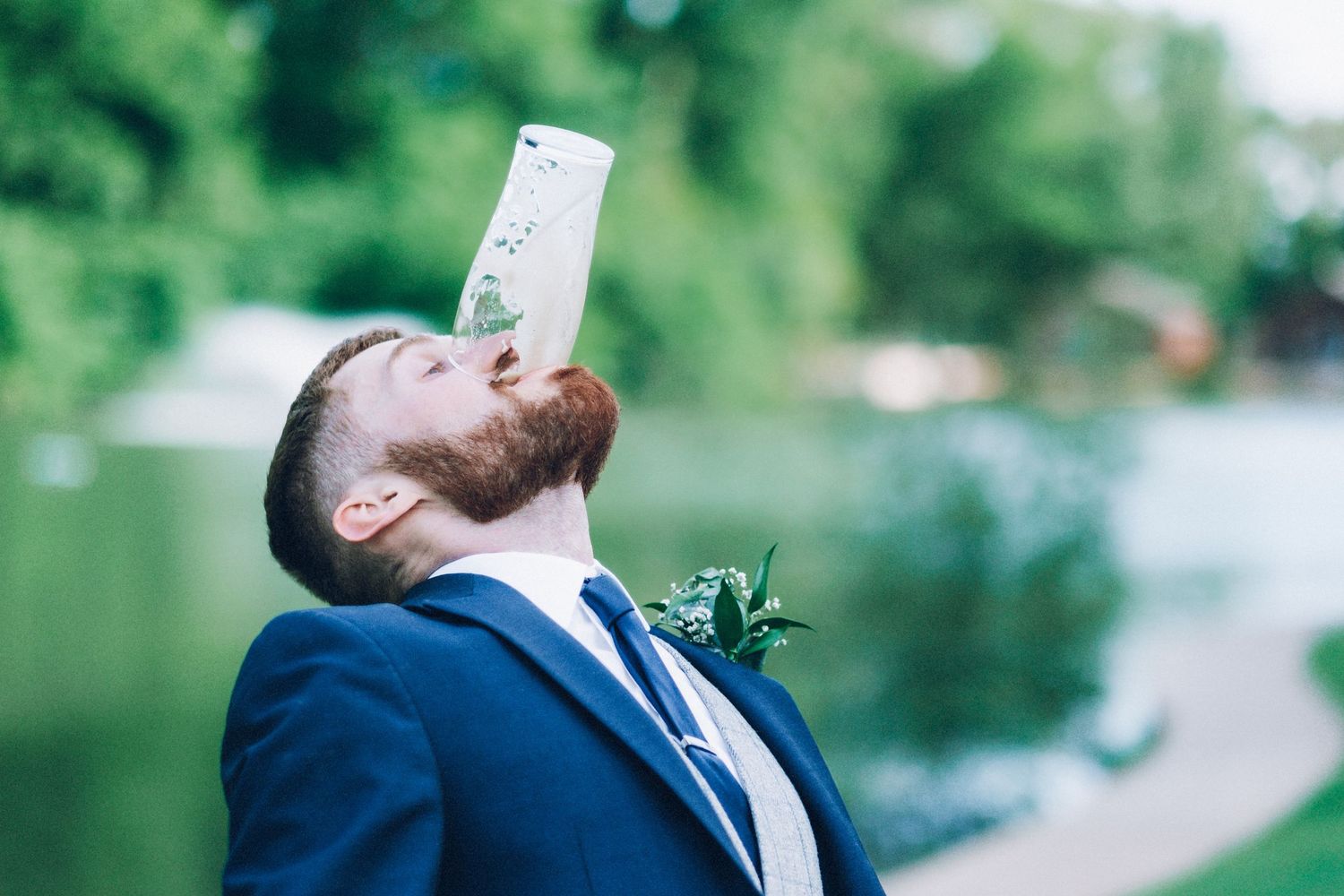 A person in a navy suit holds up a piece of paper near a lake setting.