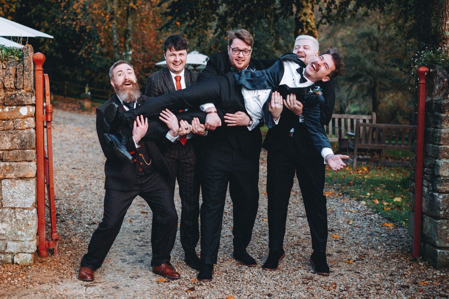 Groom and groomsmen strike playful poses together on a gravel path in an outdoor setting.