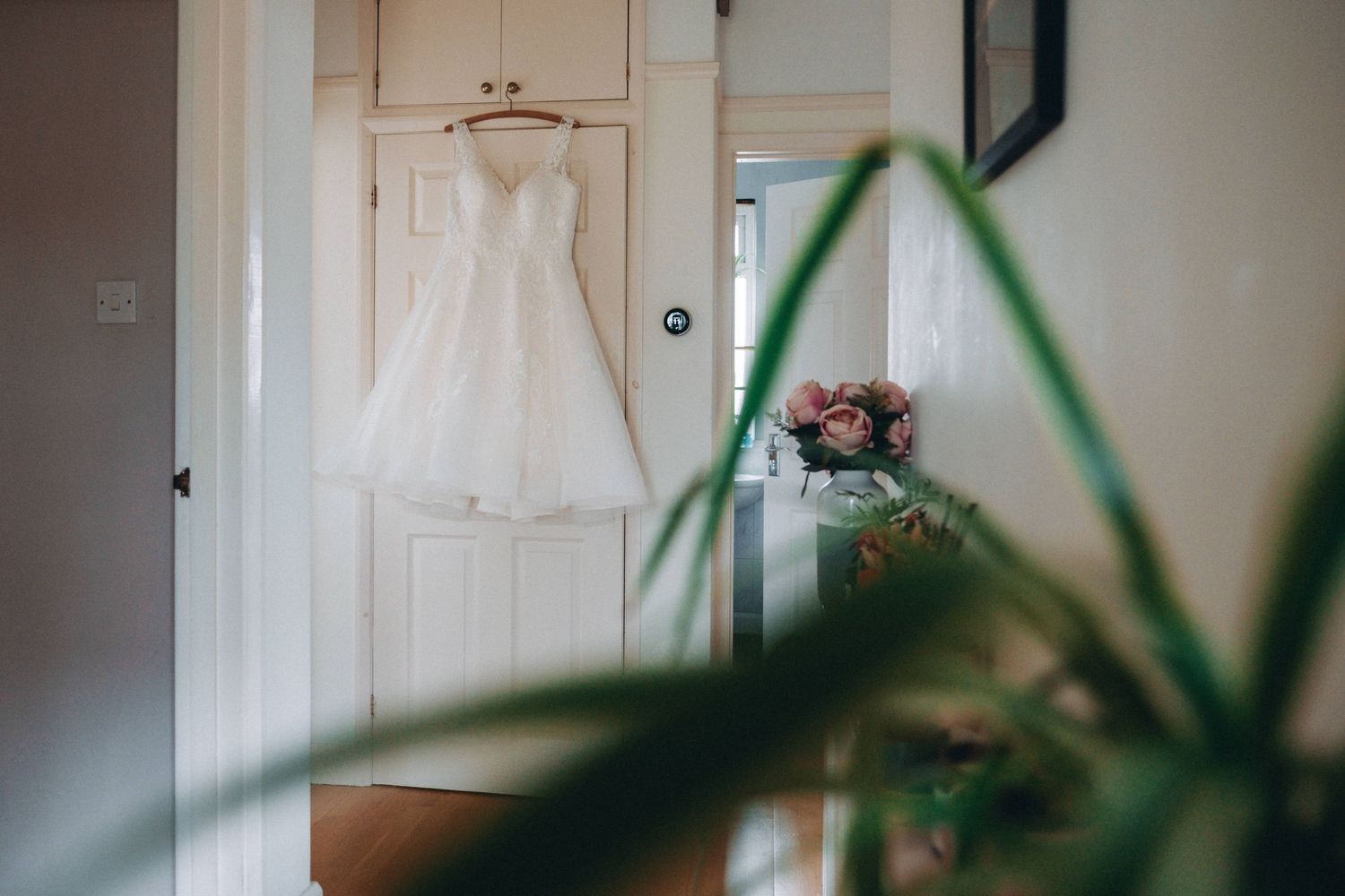 White wedding dress hanging from wooden door with greenery in foreground creating soft, ethereal scene. South Devon Wedding Photographer.