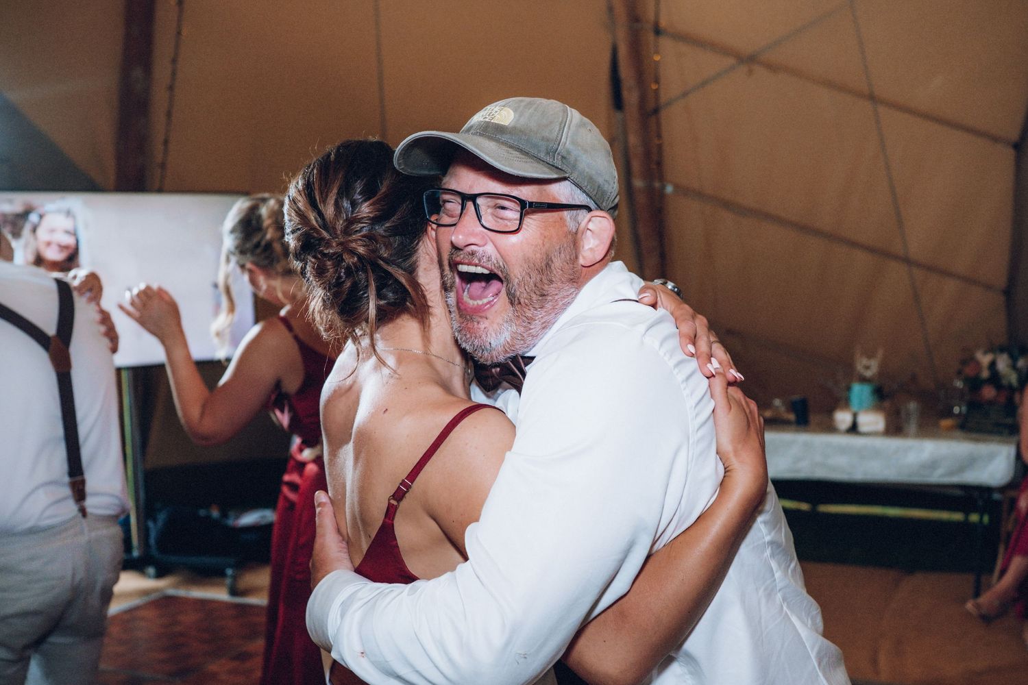 Wedding reception guests dance and celebrate under warm tent lighting.
