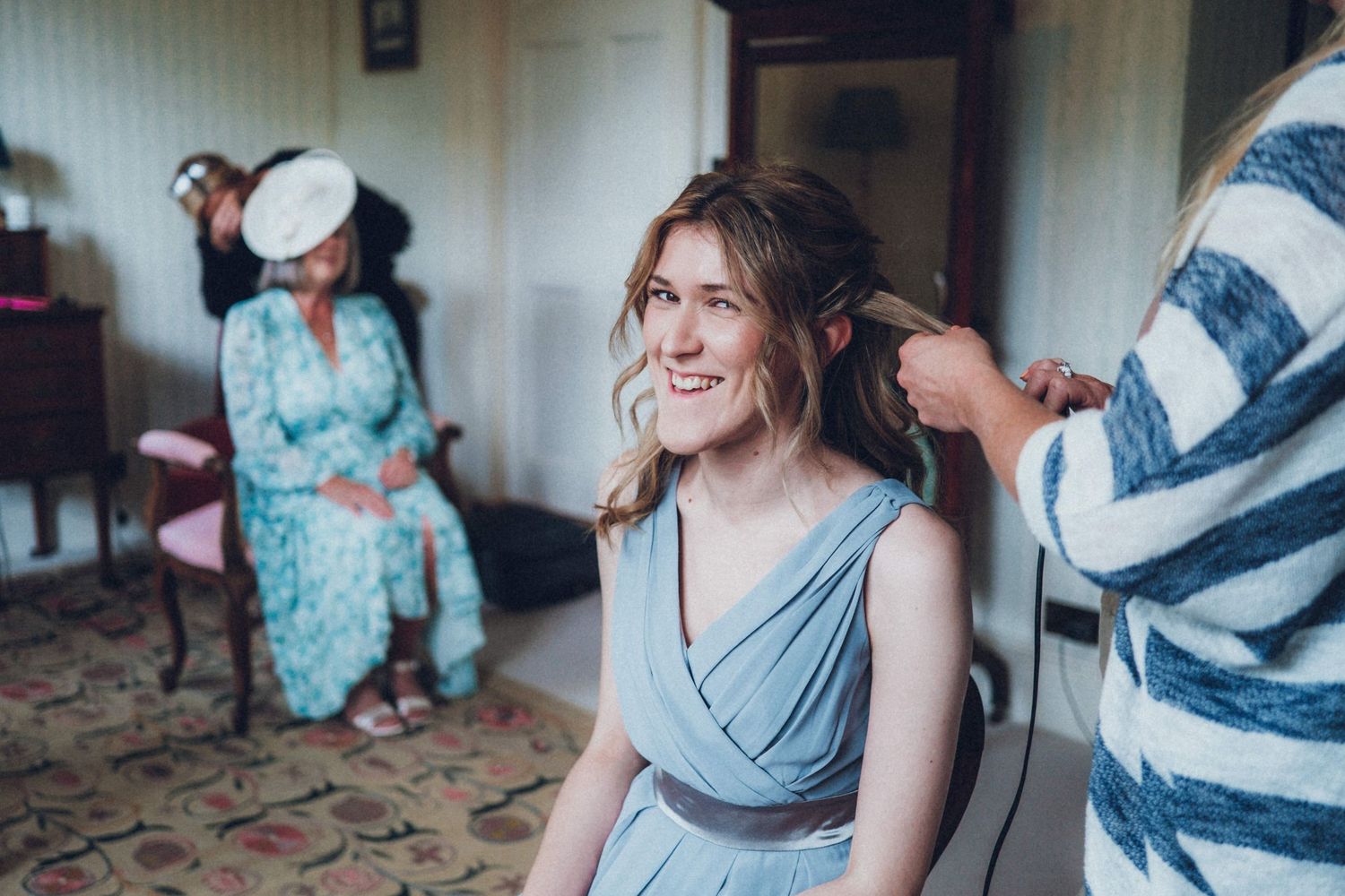 Wedding preparation scene with bridesmaids and stylists working on hair and makeup.