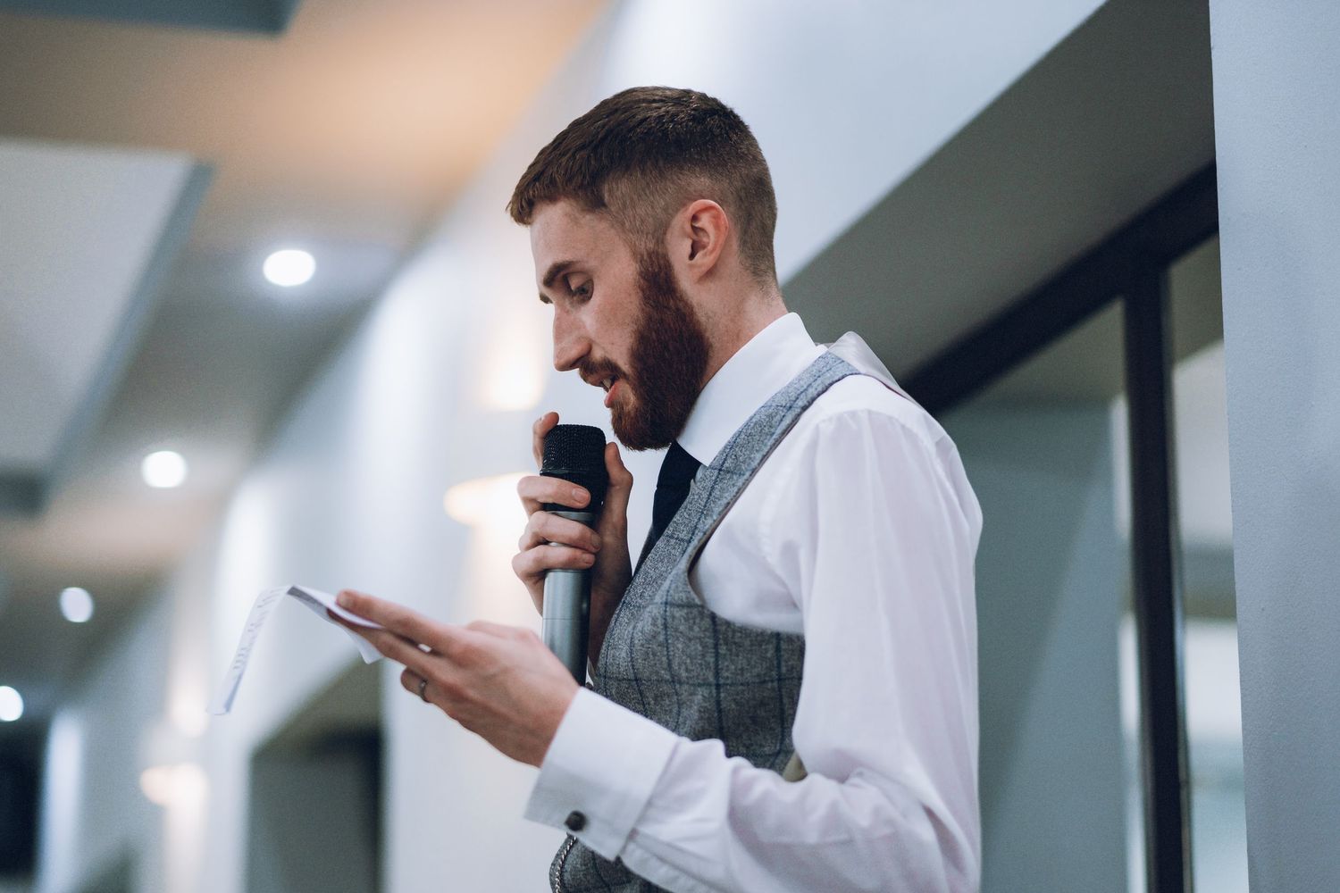 A person in formal attire speaks into a microphone while holding notes.