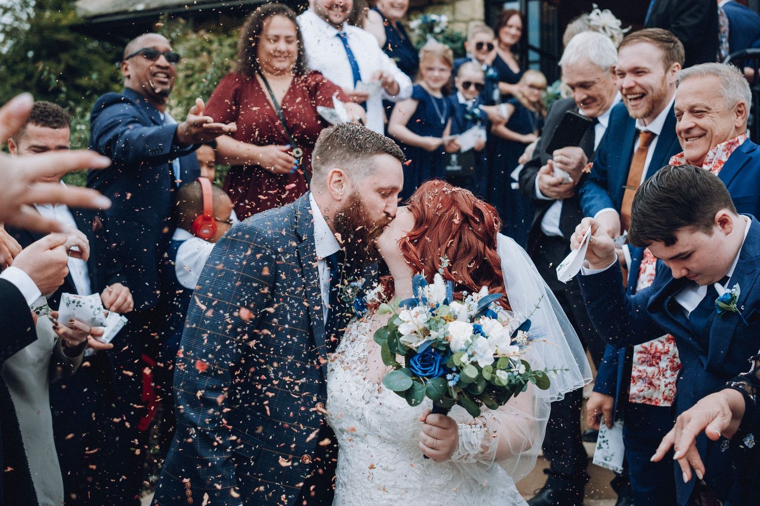 Wedding guests throw confetti as the newlyweds walk through an outdoor celebration.