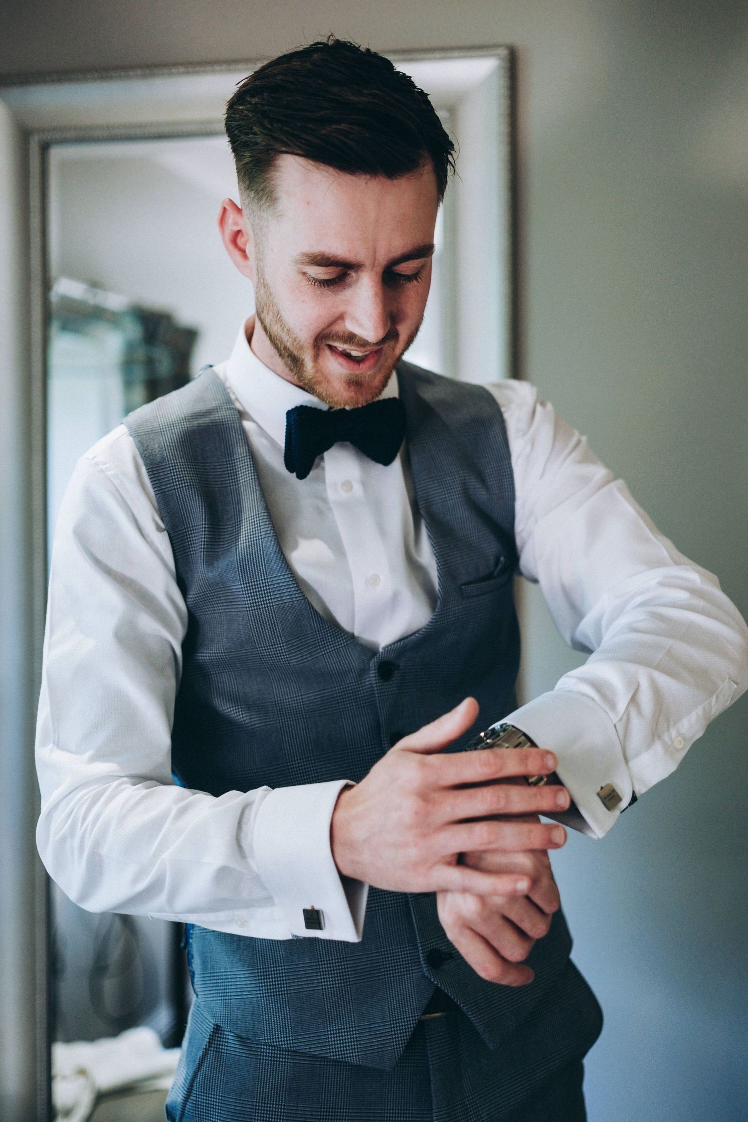 A groom in formal attire adjusts his cufflinks while getting ready for the wedding ceremony.