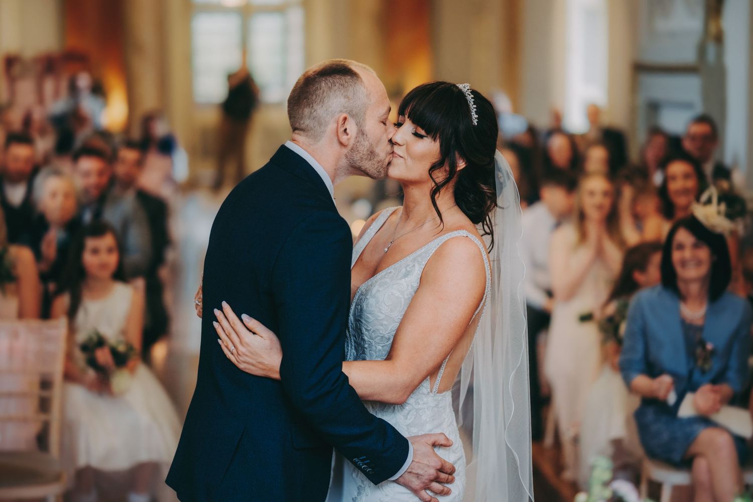 A tender moment captured during a wedding ceremony with guests in the background.
