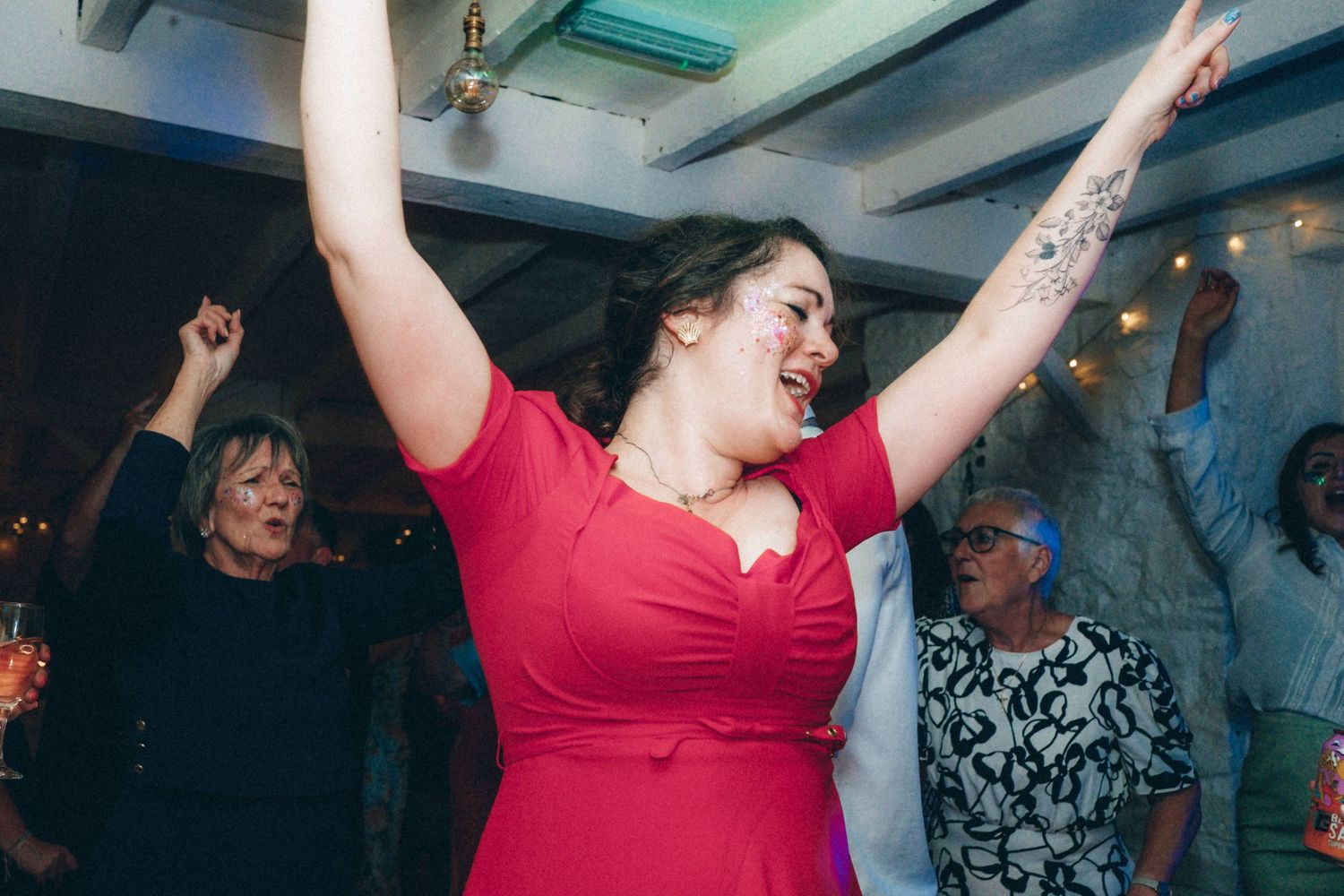 People dancing and celebrating with raised arms at an indoor party.