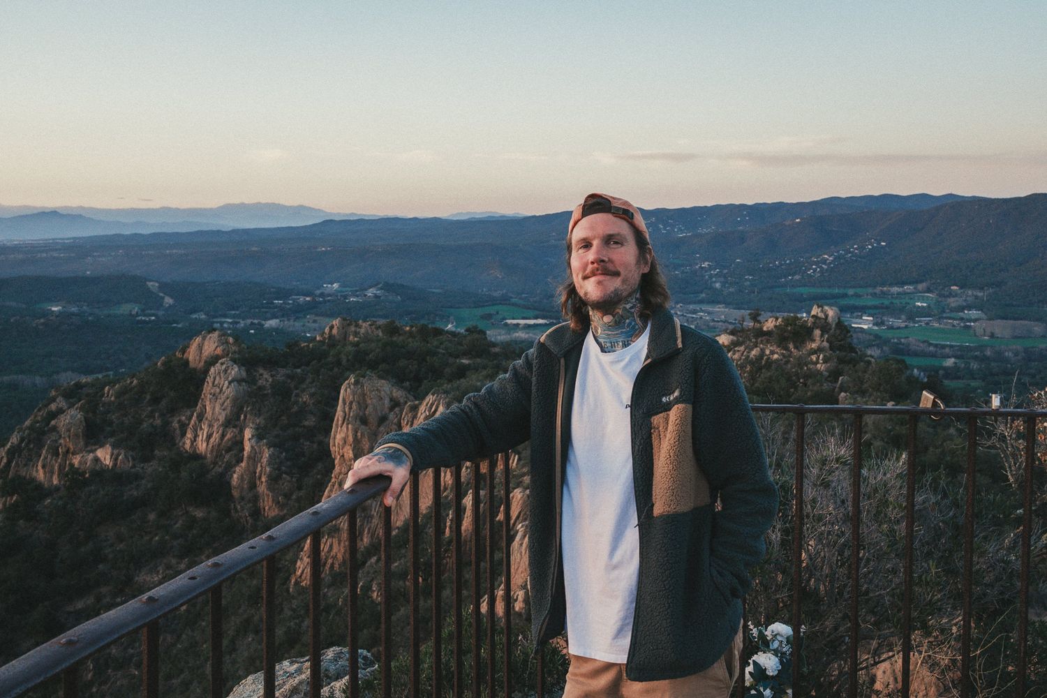 Trioh Media at scenic mountain overlook wearing brown jacket during sunset.