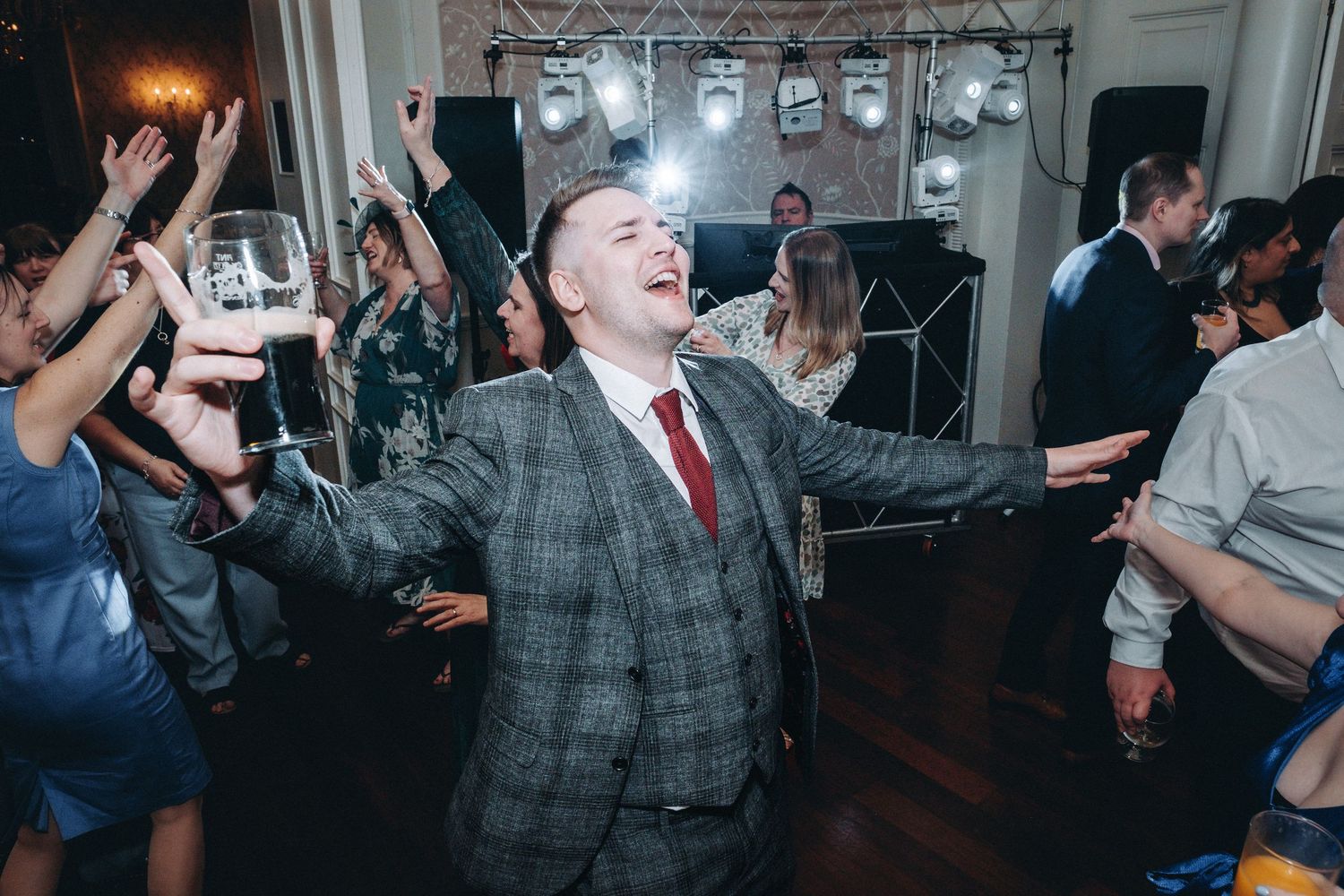 Wedding guests dancing and celebrating enthusiastically on a dark dance floor with party lighting.