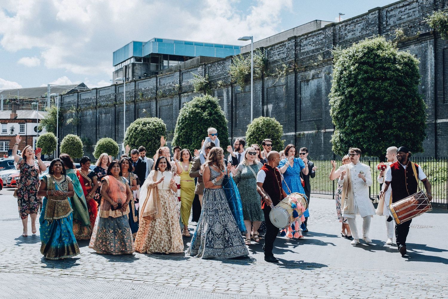 Large group of wedding guests in traditional Indian attire walking outside historic building.