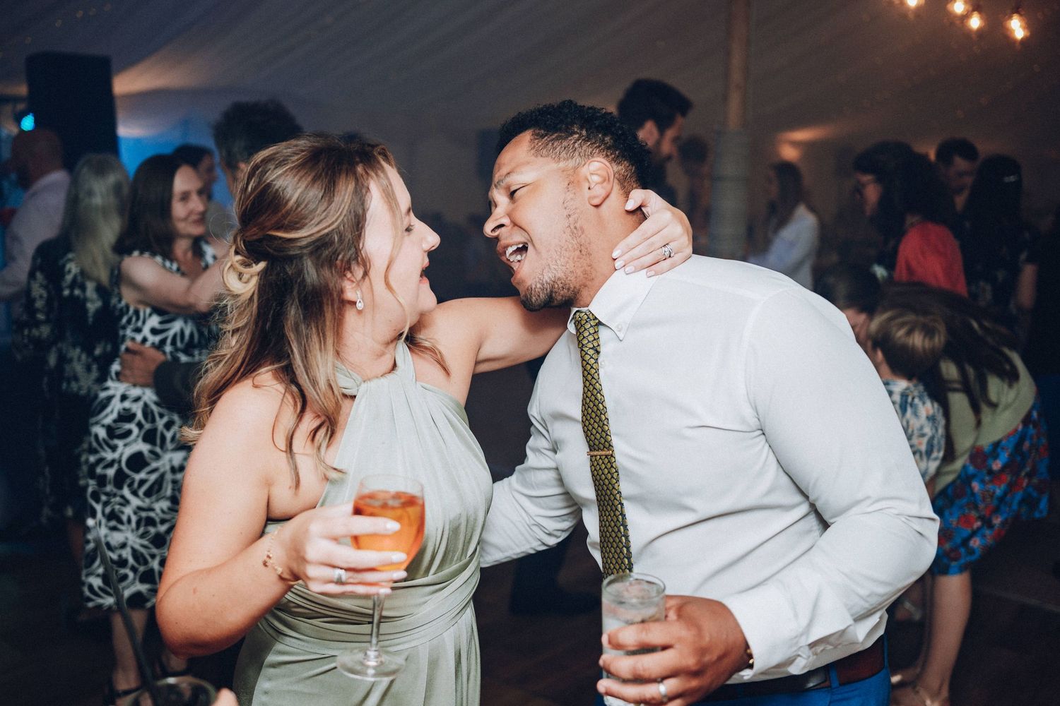 Couple sharing a romantic dance moment at a wedding reception with string lights in the background.