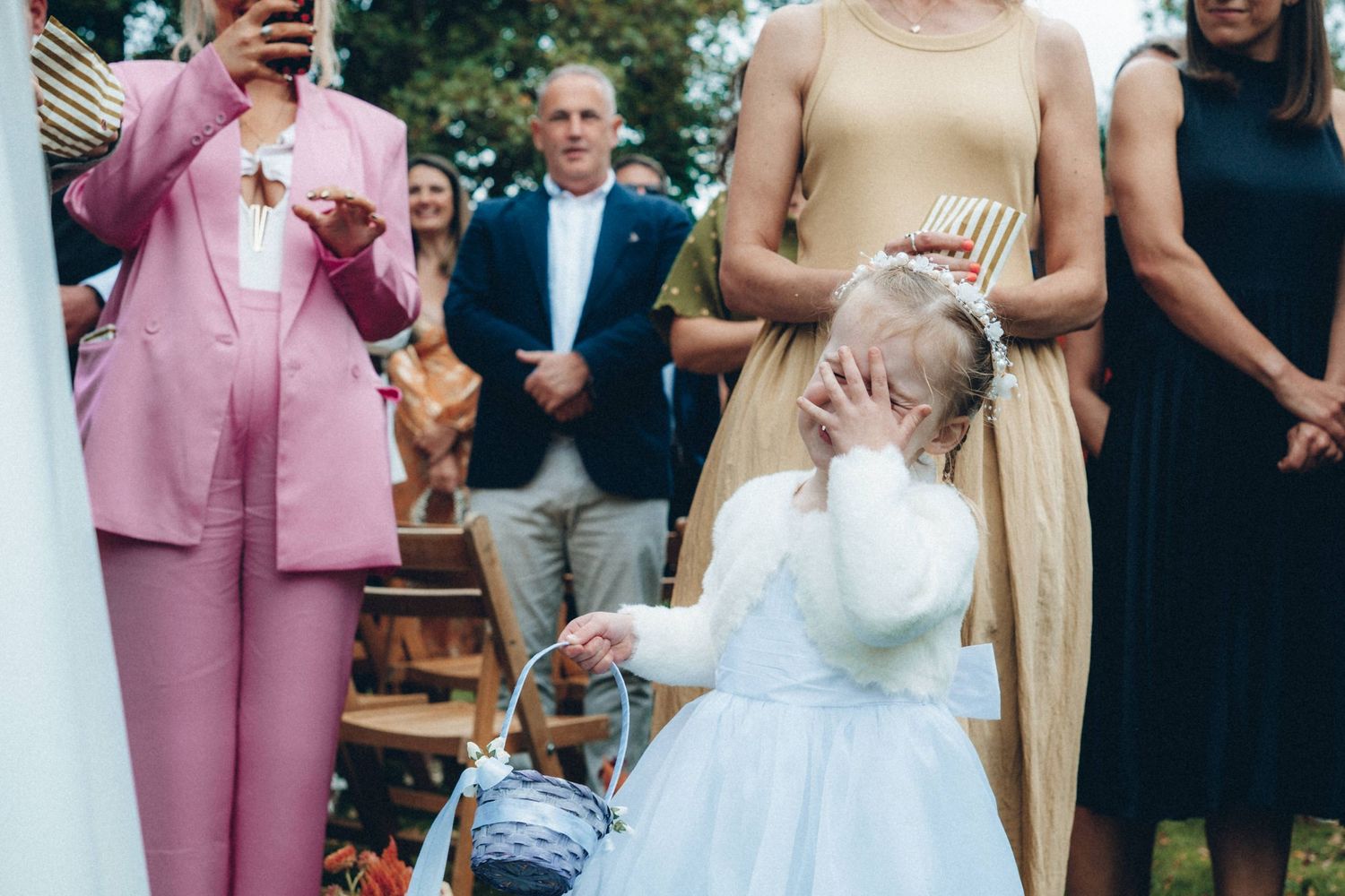 A young flower girl in white dress reacts emotionally during wedding festivities.