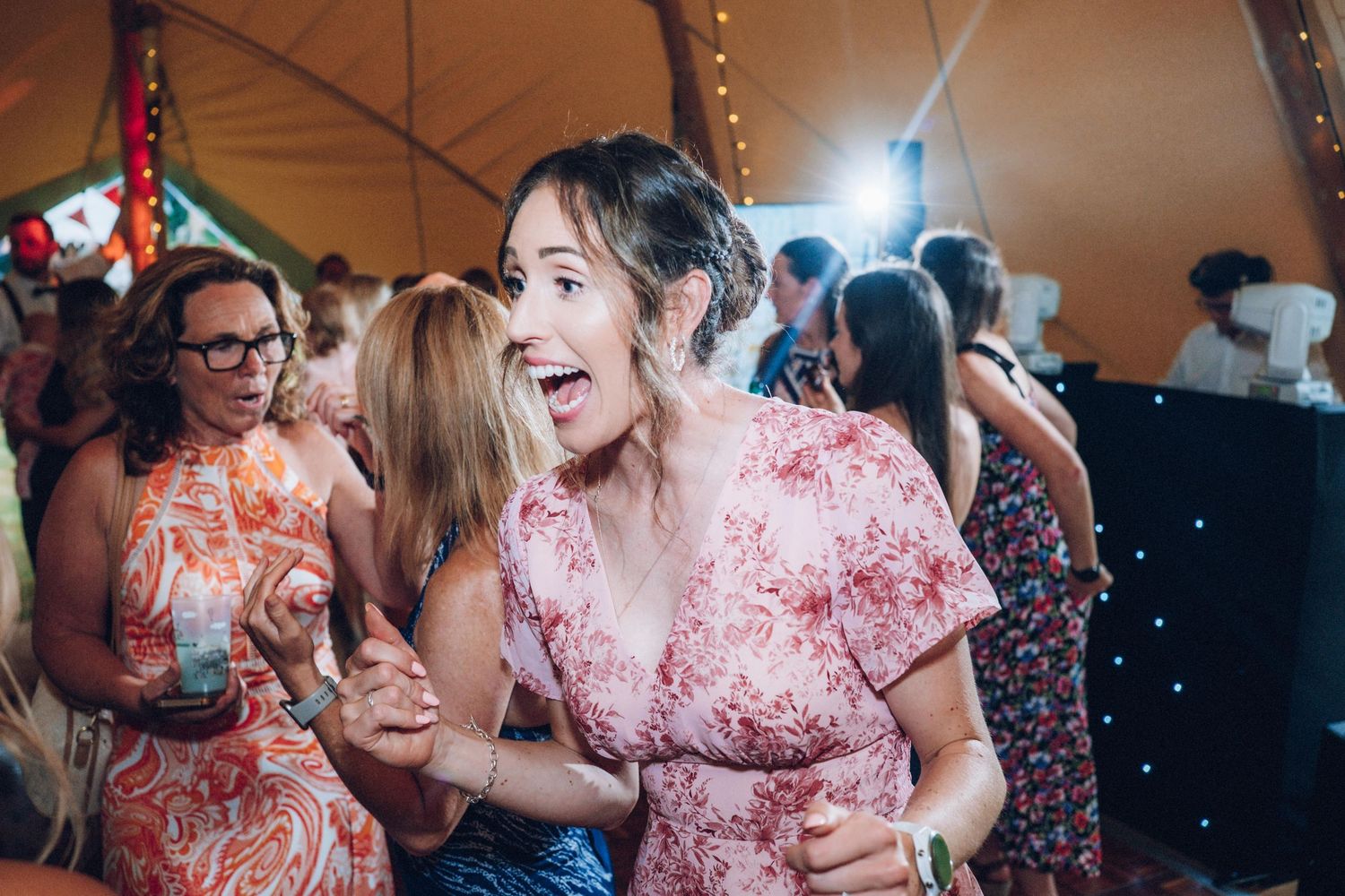 Wedding guests dancing and celebrating under string lights in a tent venue.