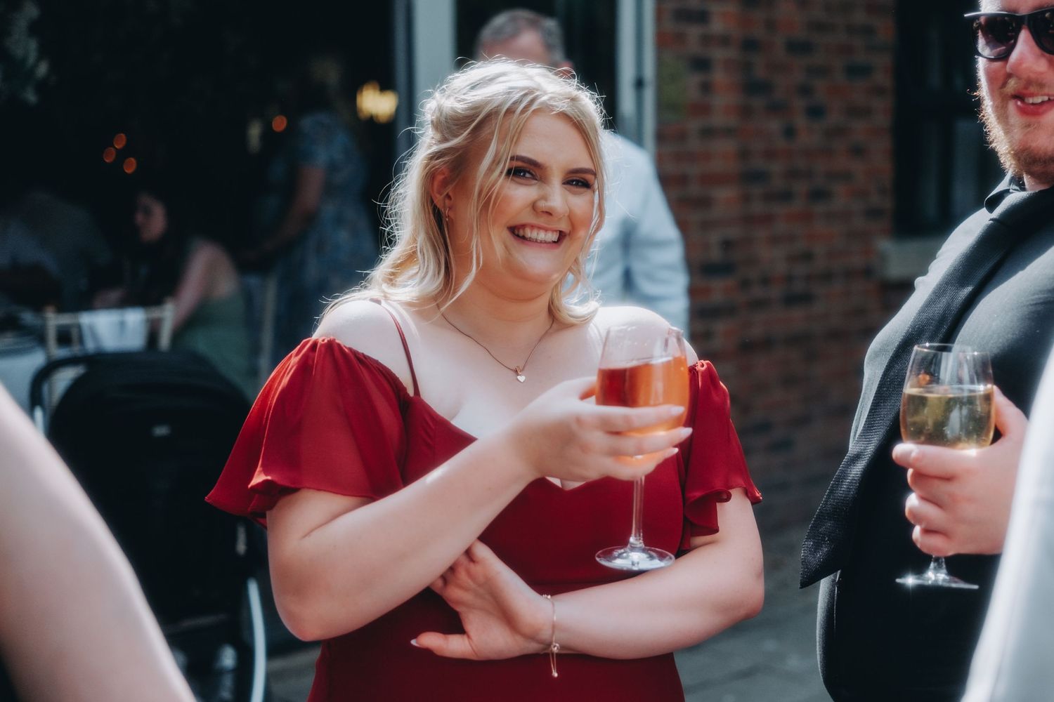 Woman in red dress holds a cocktail glass while smiling at outdoor wedding
.