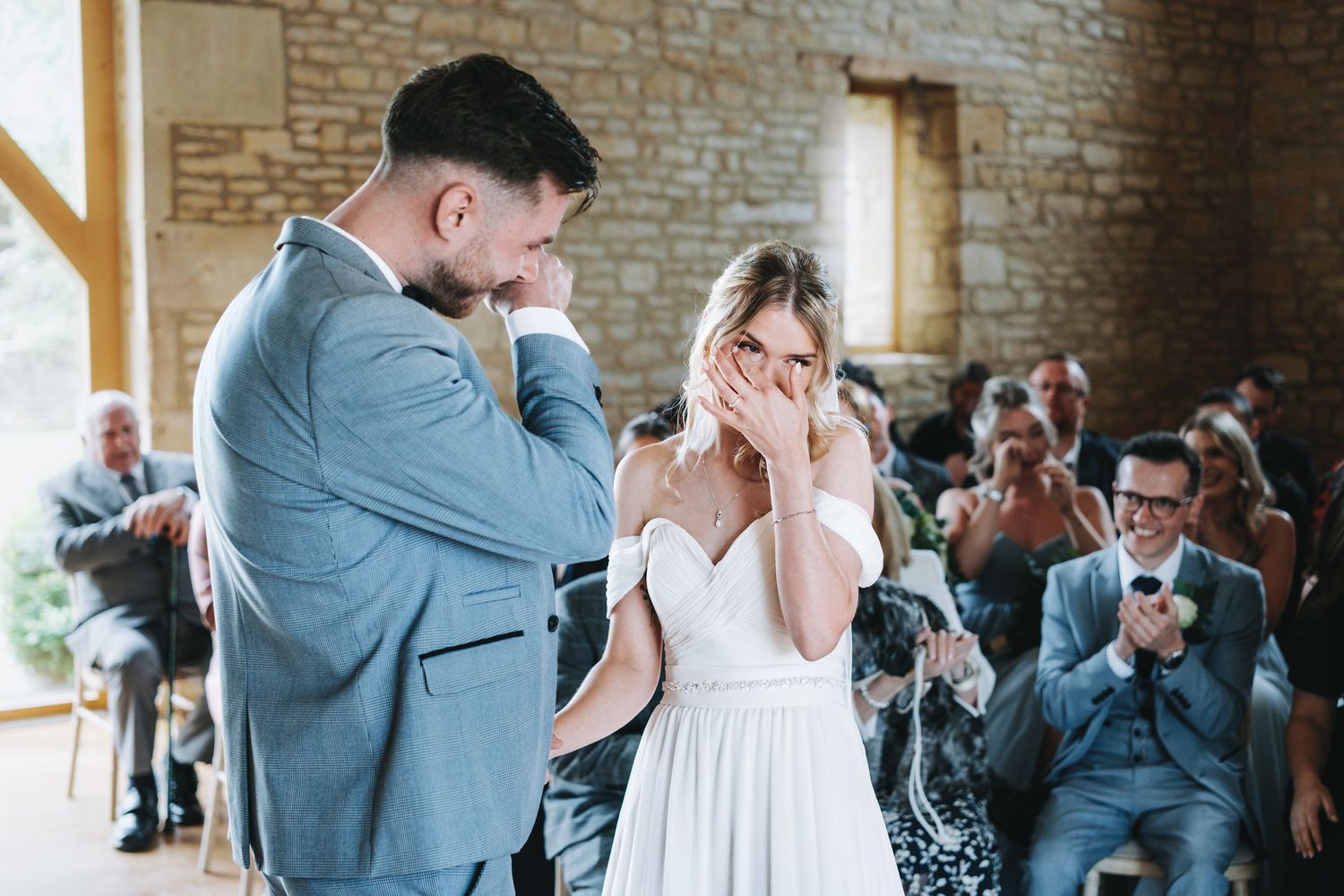 An emotional moment at a rustic indoor wedding ceremony with guests watching in the background.