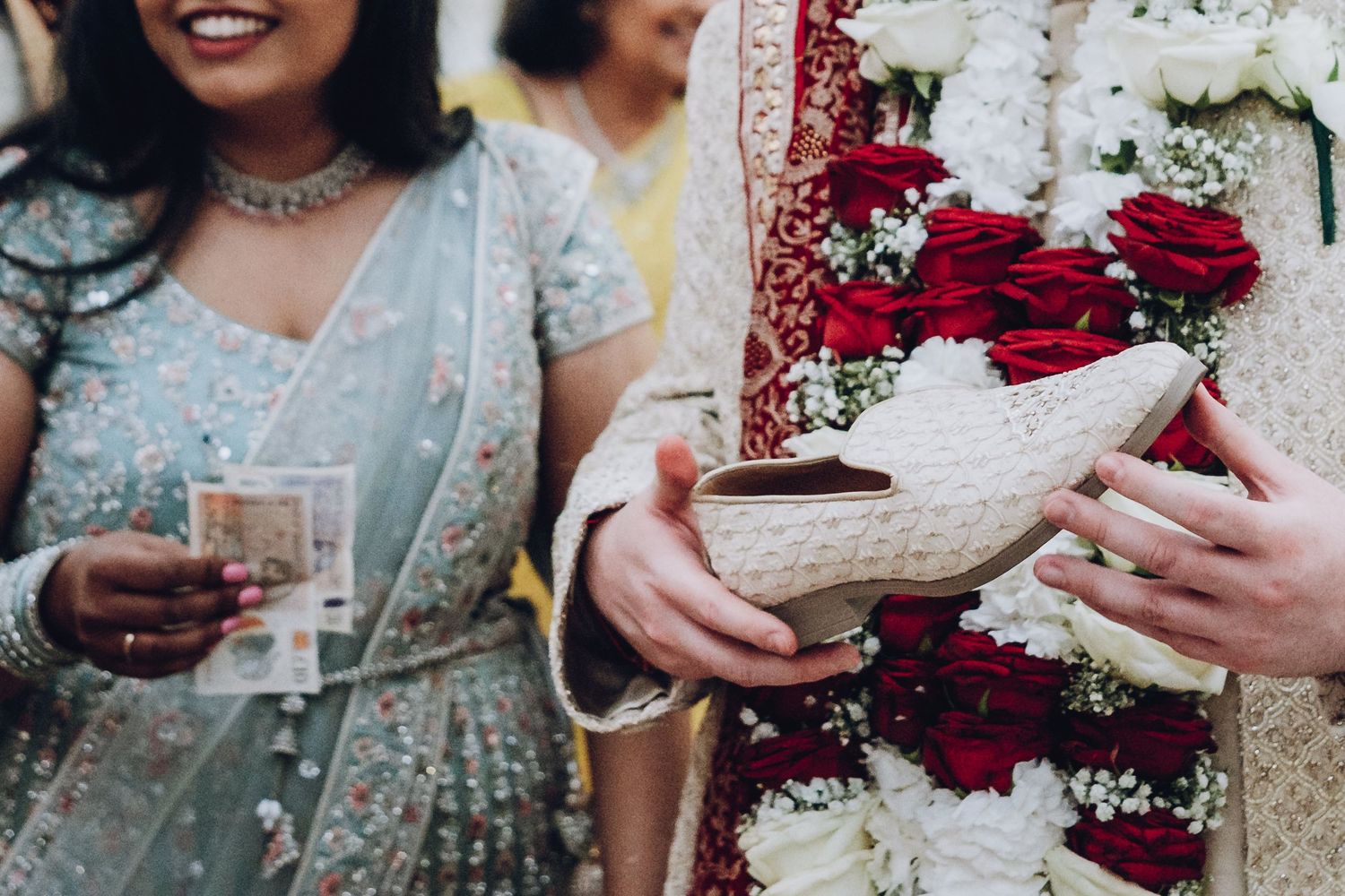 Wedding party members in traditional Indian attire hold bouquets of red flowers during celebration.