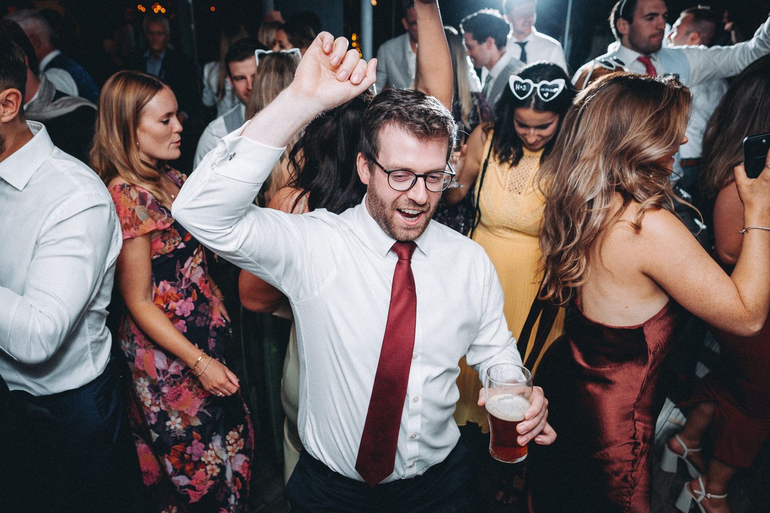 Wedding guests dancing and laughing together at a dimly lit reception venue.