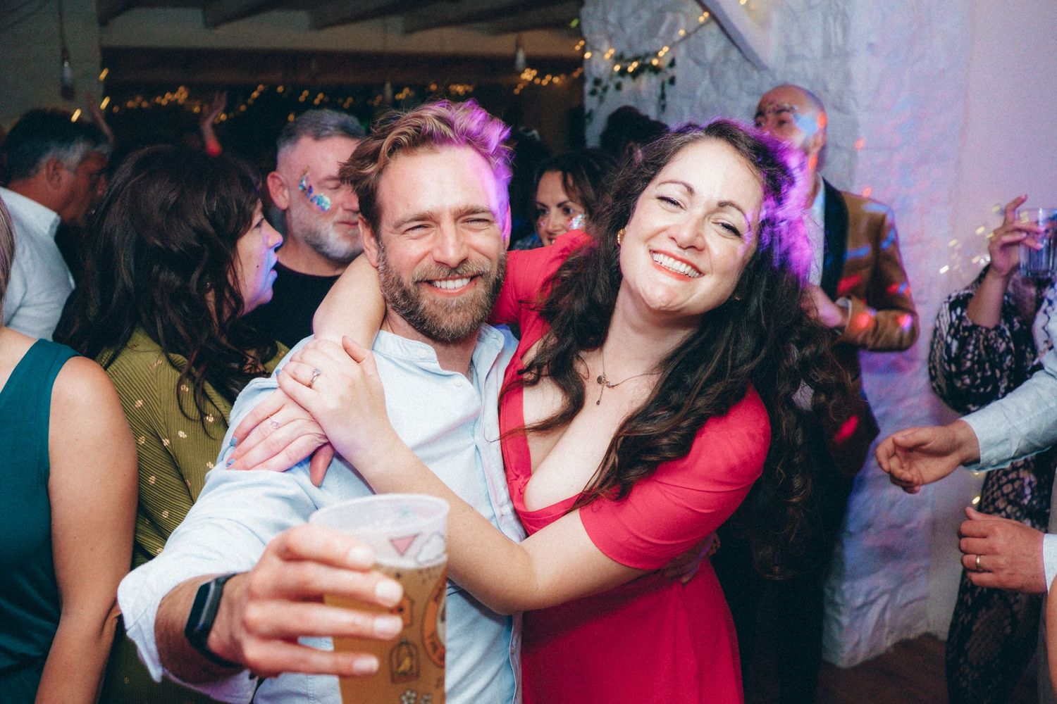 Party guests dancing and celebrating at a lively indoor event with colorful lighting.