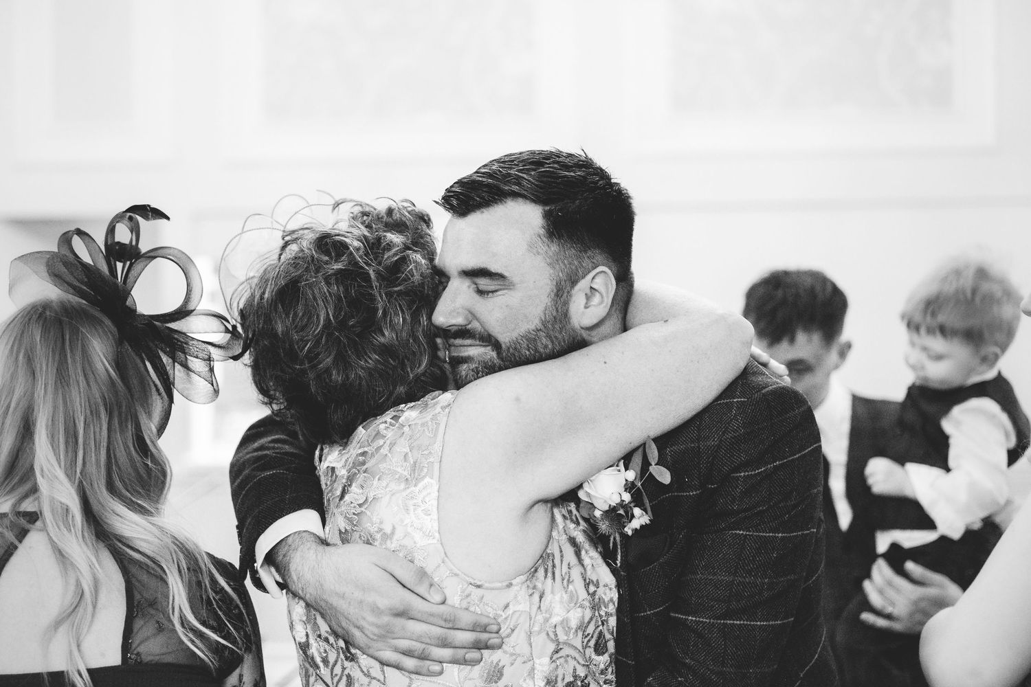 Wedding party members share hugs and emotional moments in bright indoor setting.