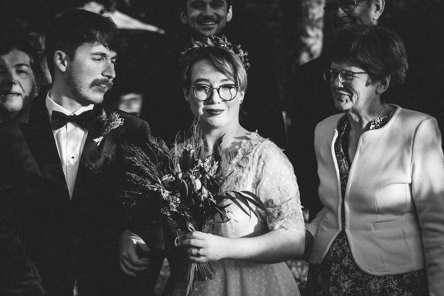Black and white candid shot of a wedding party holding a bouquet of dried flowers.