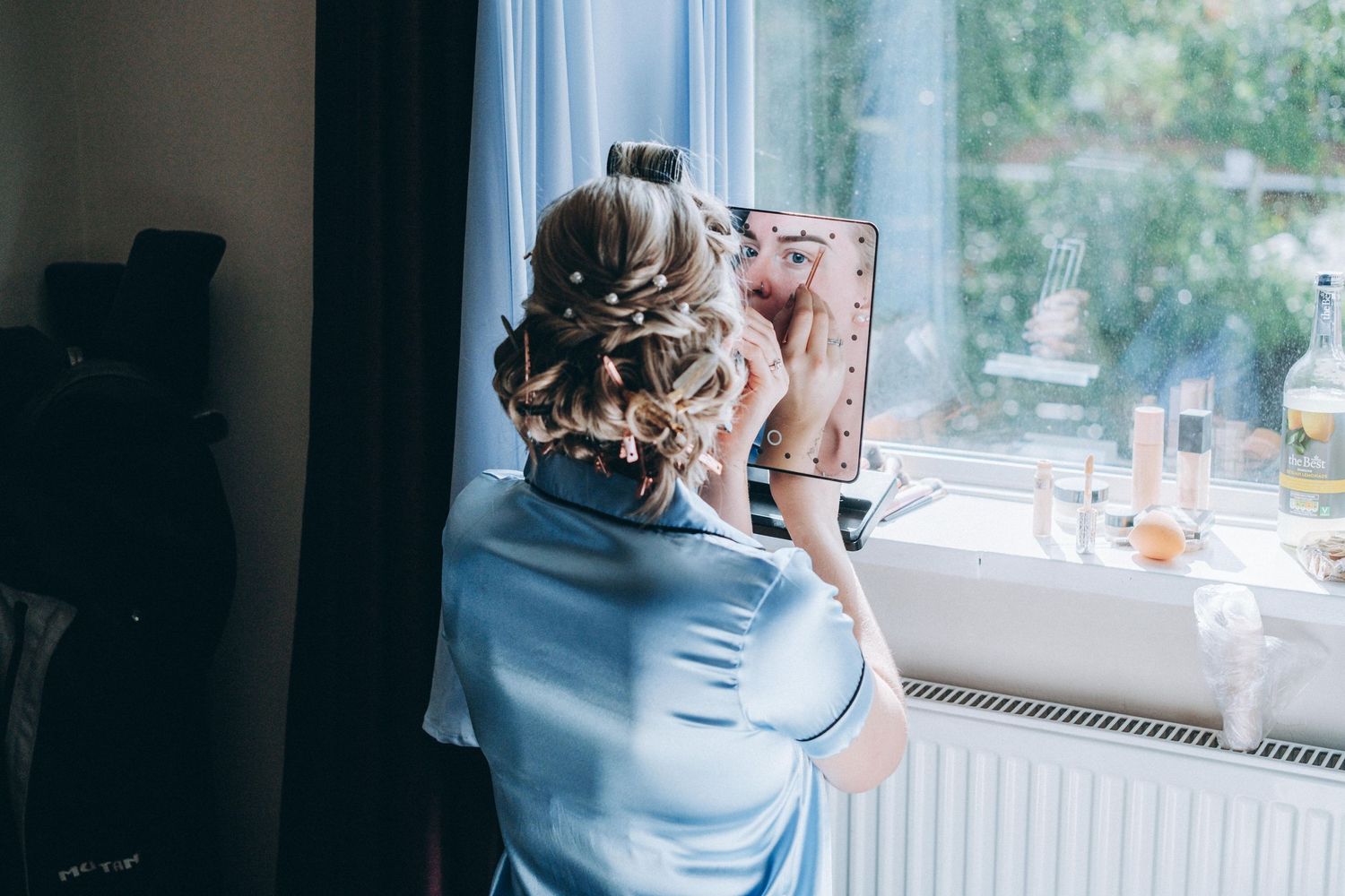 Wedding hair stylist works on an elegant updo hairstyle by a window in natural lighting.