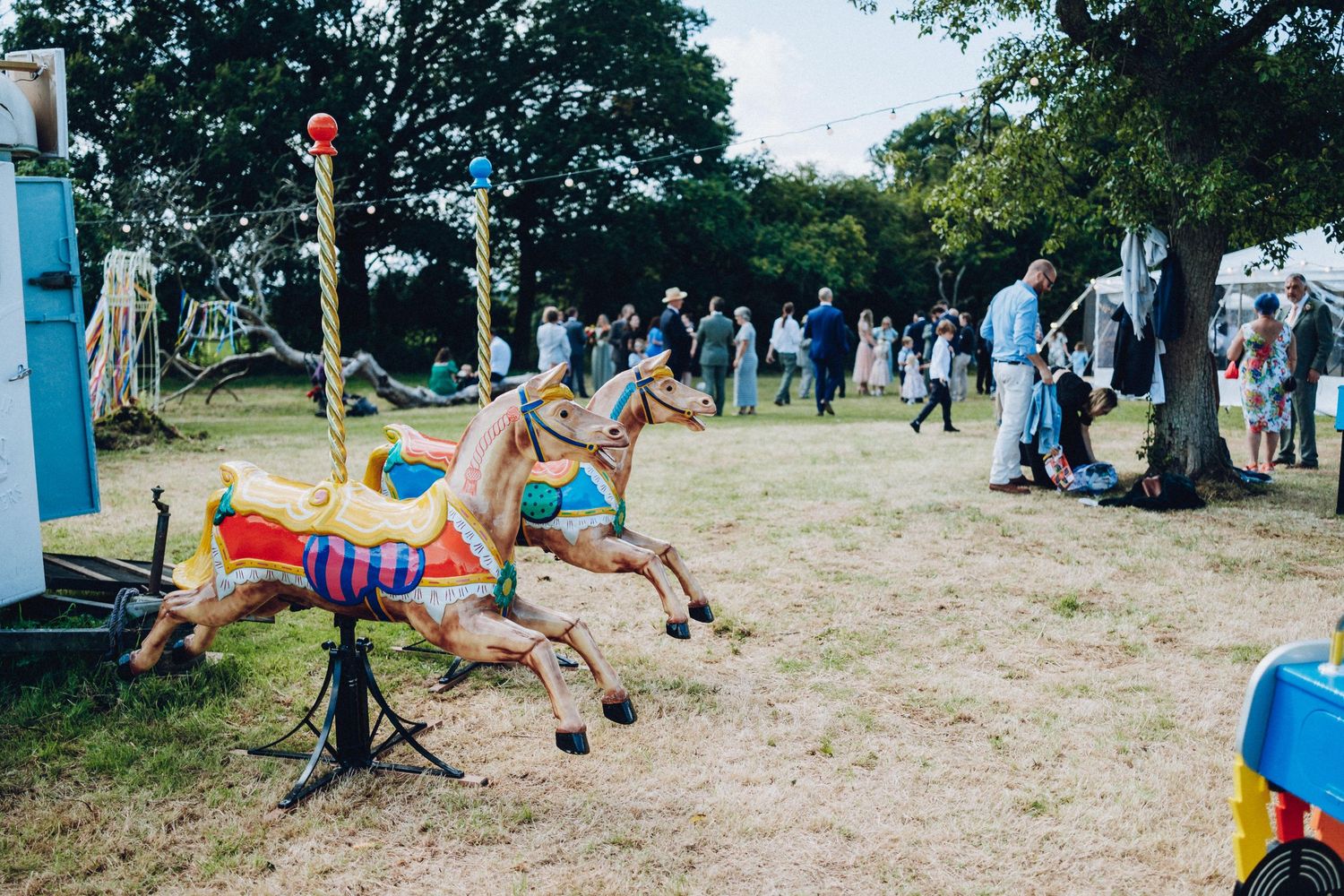 Panoramic view of an outdoor event space with trees and scattered guests enjoying activities.